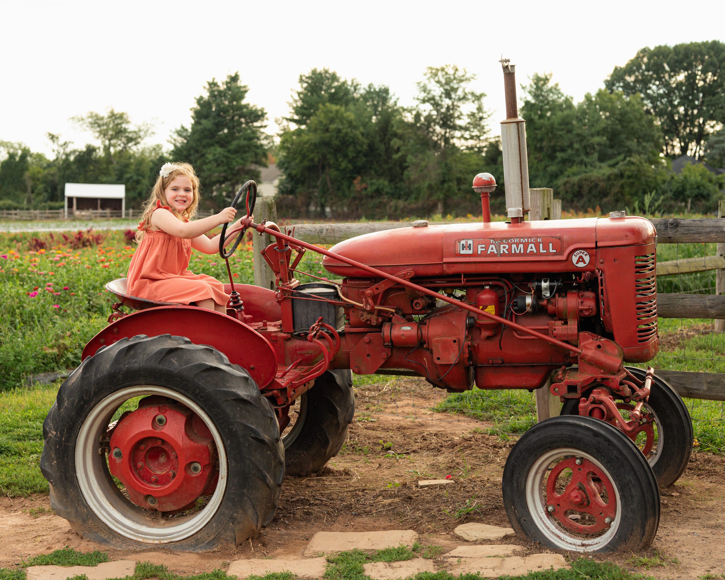 a young girl sitting on an antique red tractor with a field of colorful flowers in the background during a philadelphia family photoshoot