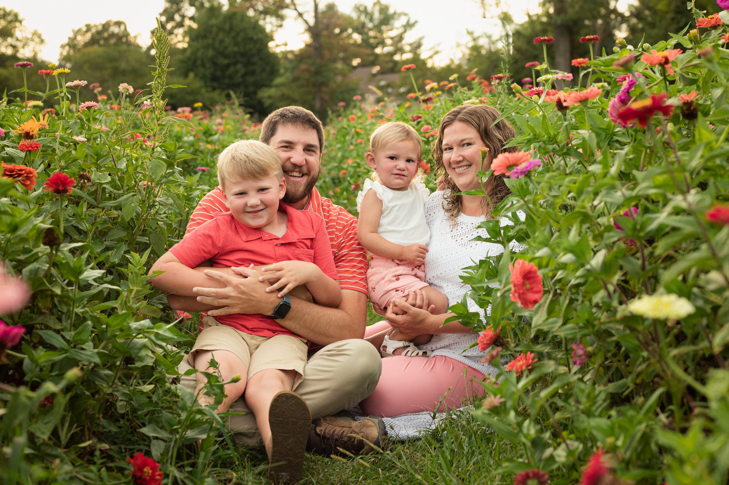 a family of four sitting in a field of colorful flowers and smiling at the camera during a philadelphia family photoshoot