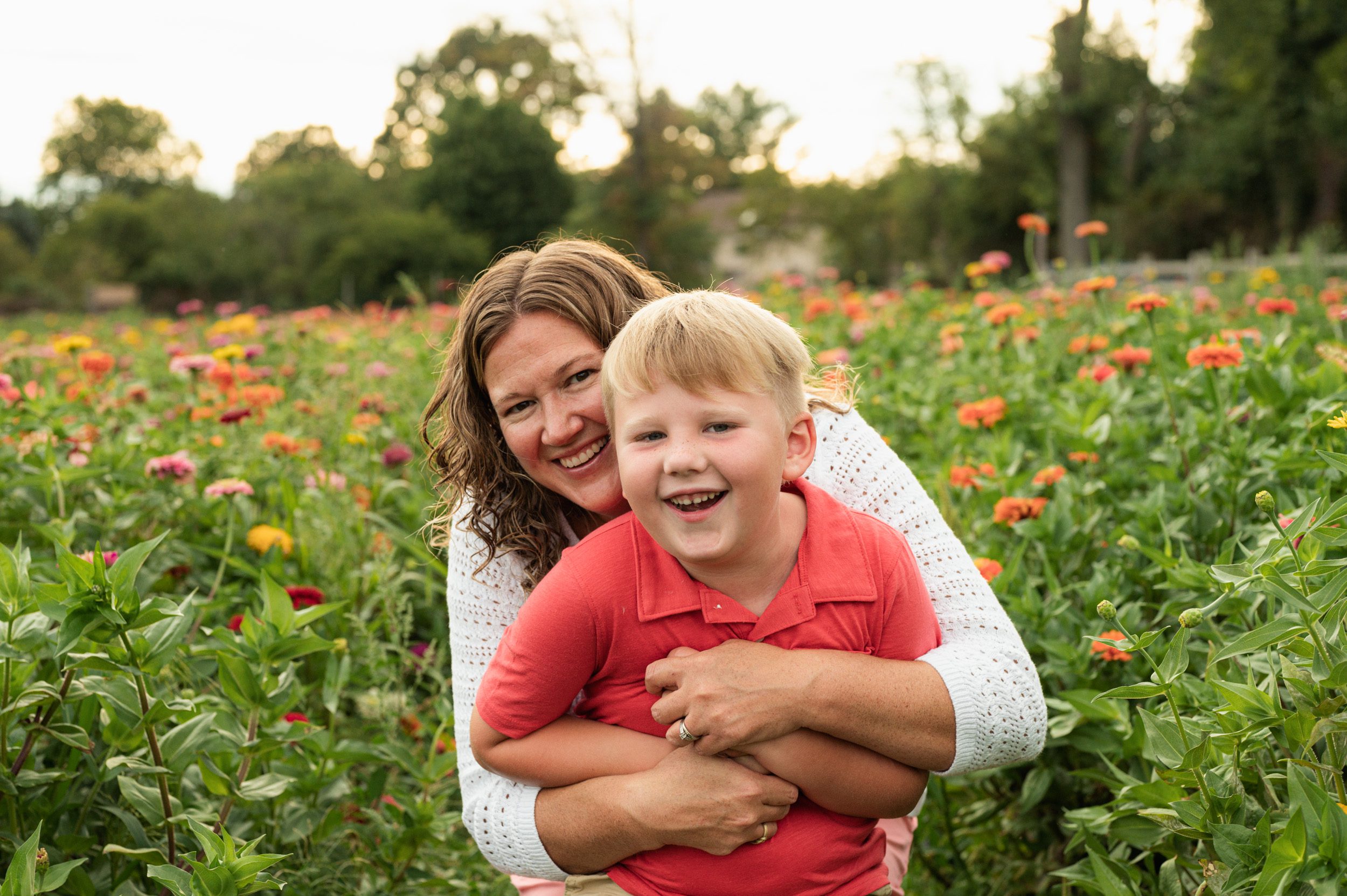 a mom hugging her son from behind in a field of colorful flowers and laughing during a family photoshoot