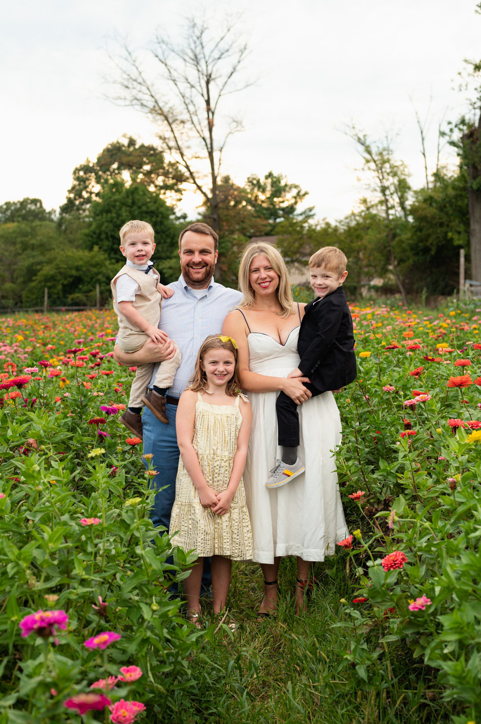a family of five standing in a field of colorful flowers and smiling at the camera during a family photoshoot