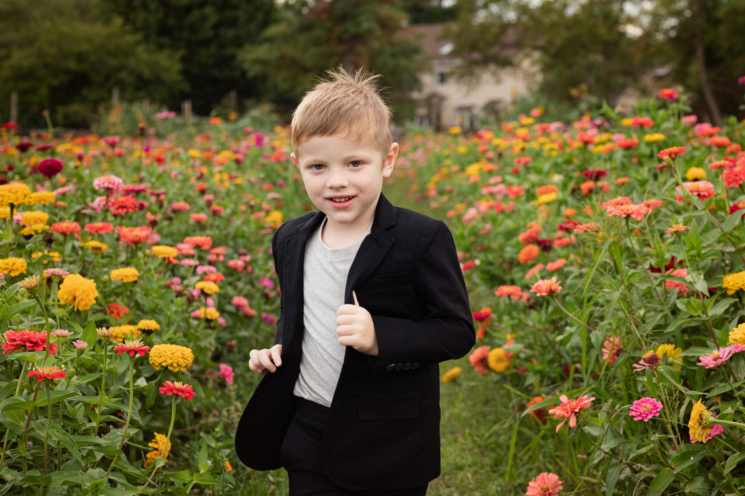 a young boy running through a field of colorful flowers and smiling at the camera during a family photoshoot