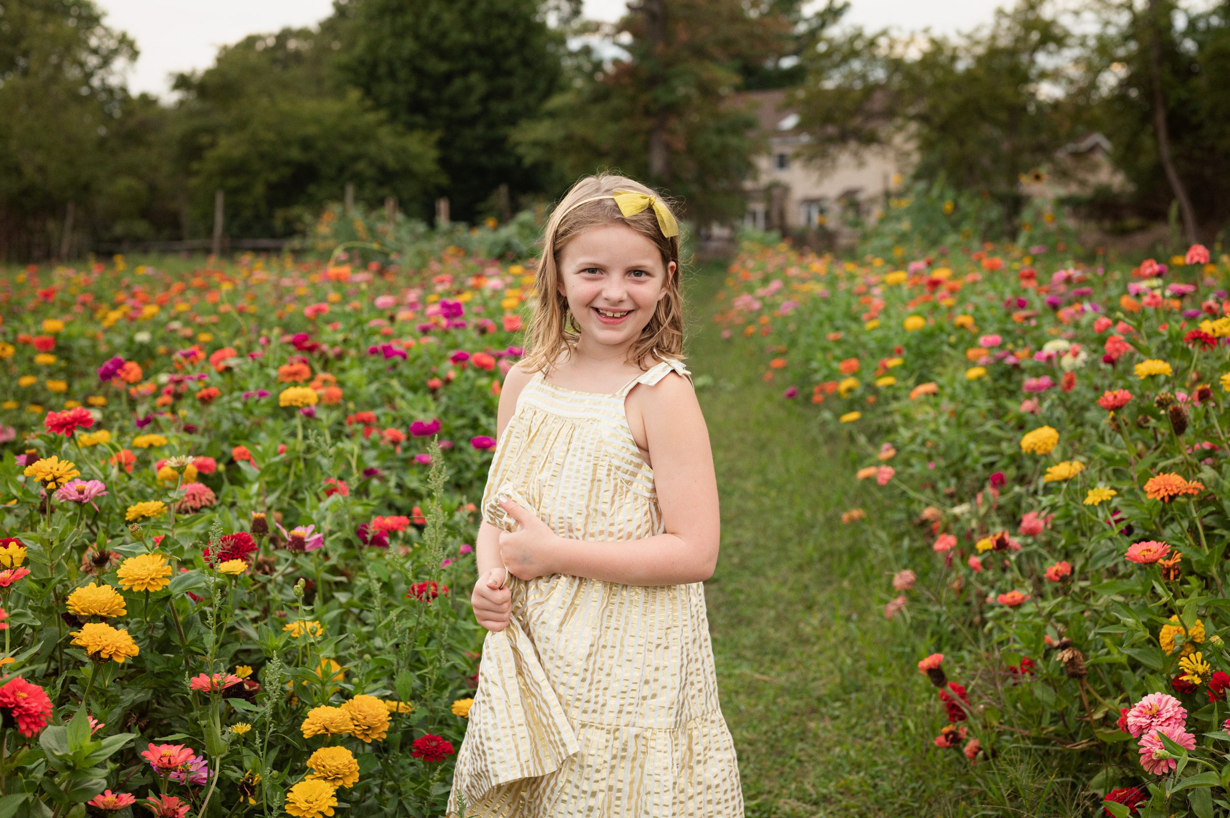 a young girl standing in a field of colorful flowers and smiling at the camera during a family photo session