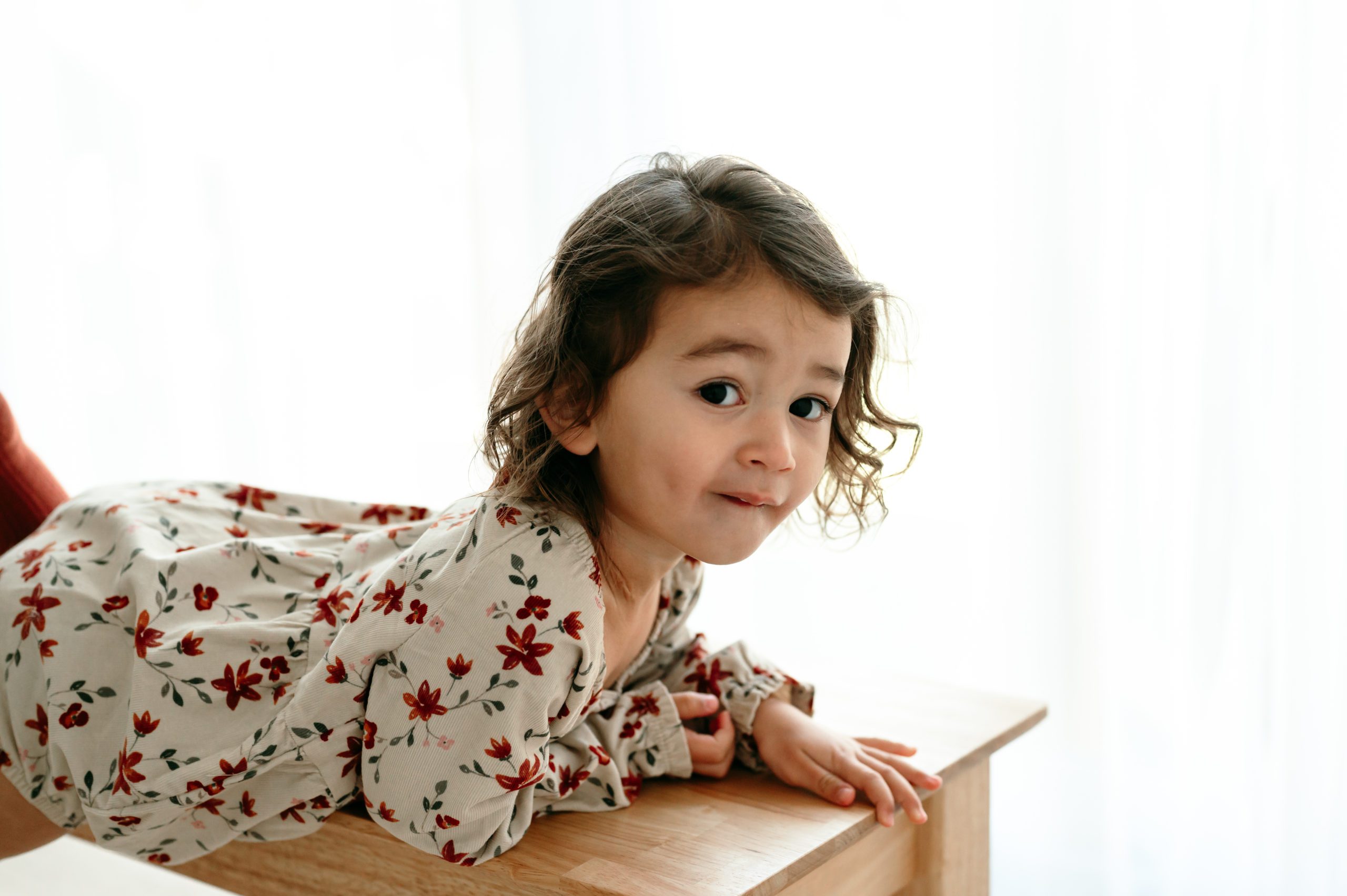 a backlit picture of a young girl climbing onto a wooden stool during a natural light studio milestone photo session