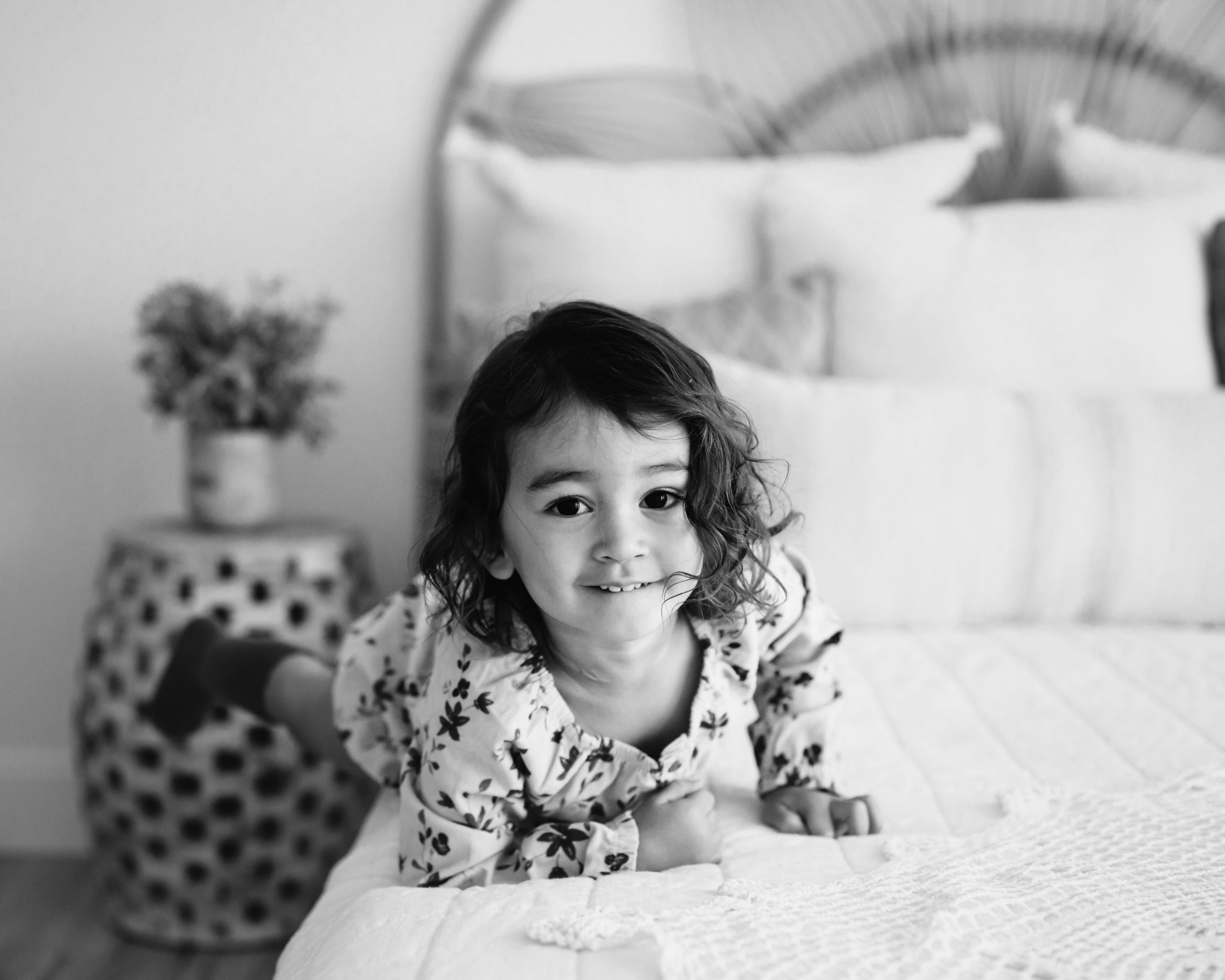 a black and white photo of a little girl climbing onto a bed during a natural light studio milestone photo session