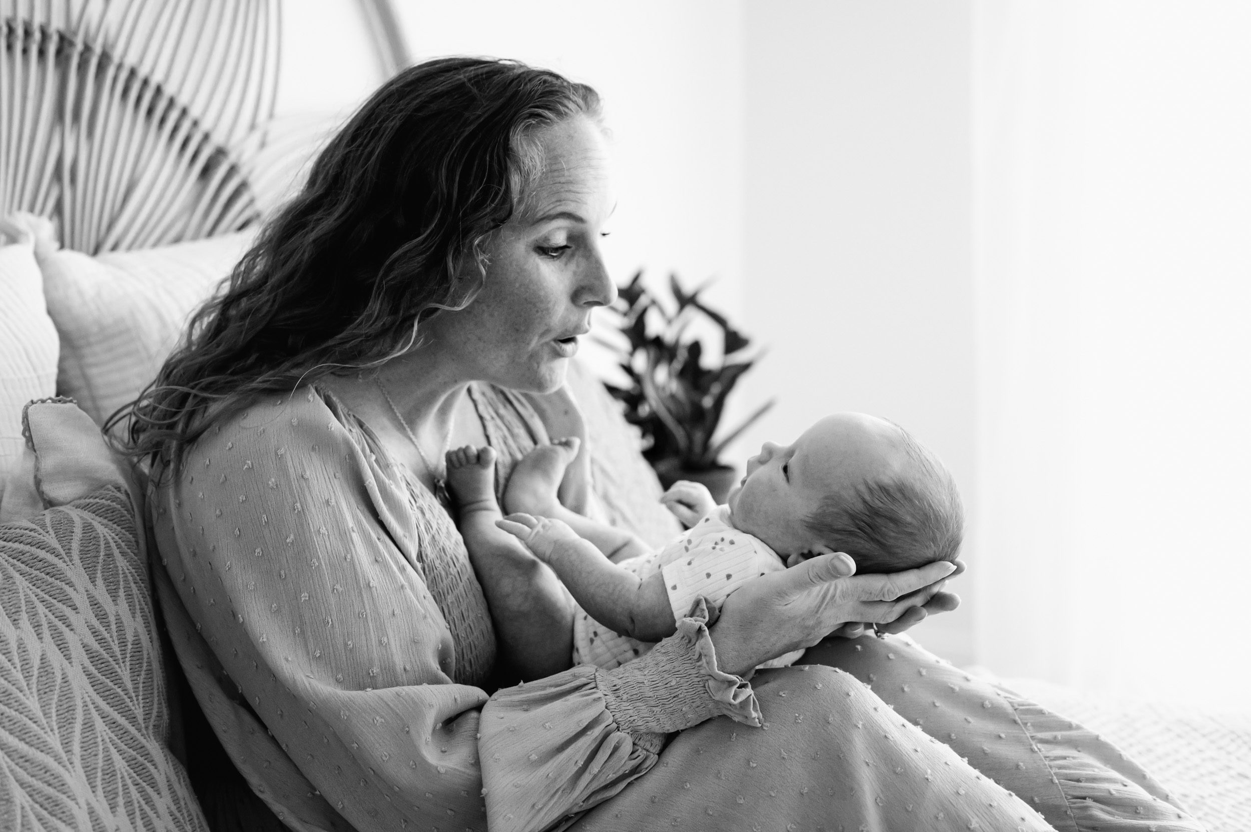 a black and white picture of a new mother holding her newborn son on her lap as they smile at each other during a newborn photo session
