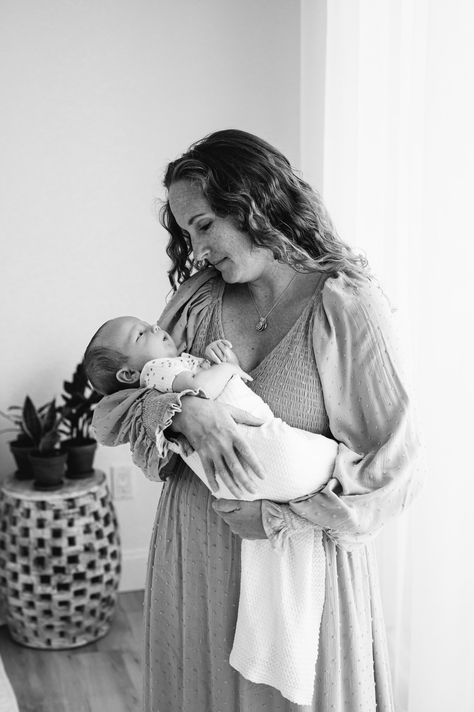 a black and white picture of a mom cradling her newborn son in her arms and smiling down at him during a natural light newborn photo session