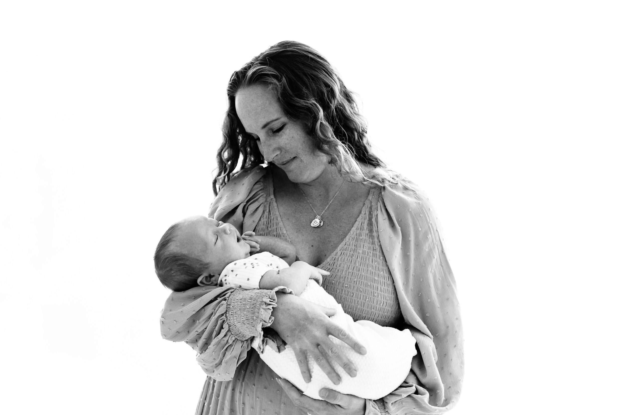 a black and white backlit image of a new mom cradling her newborn son in her arms and smiling down at him during a natural light newborn photoshoot
