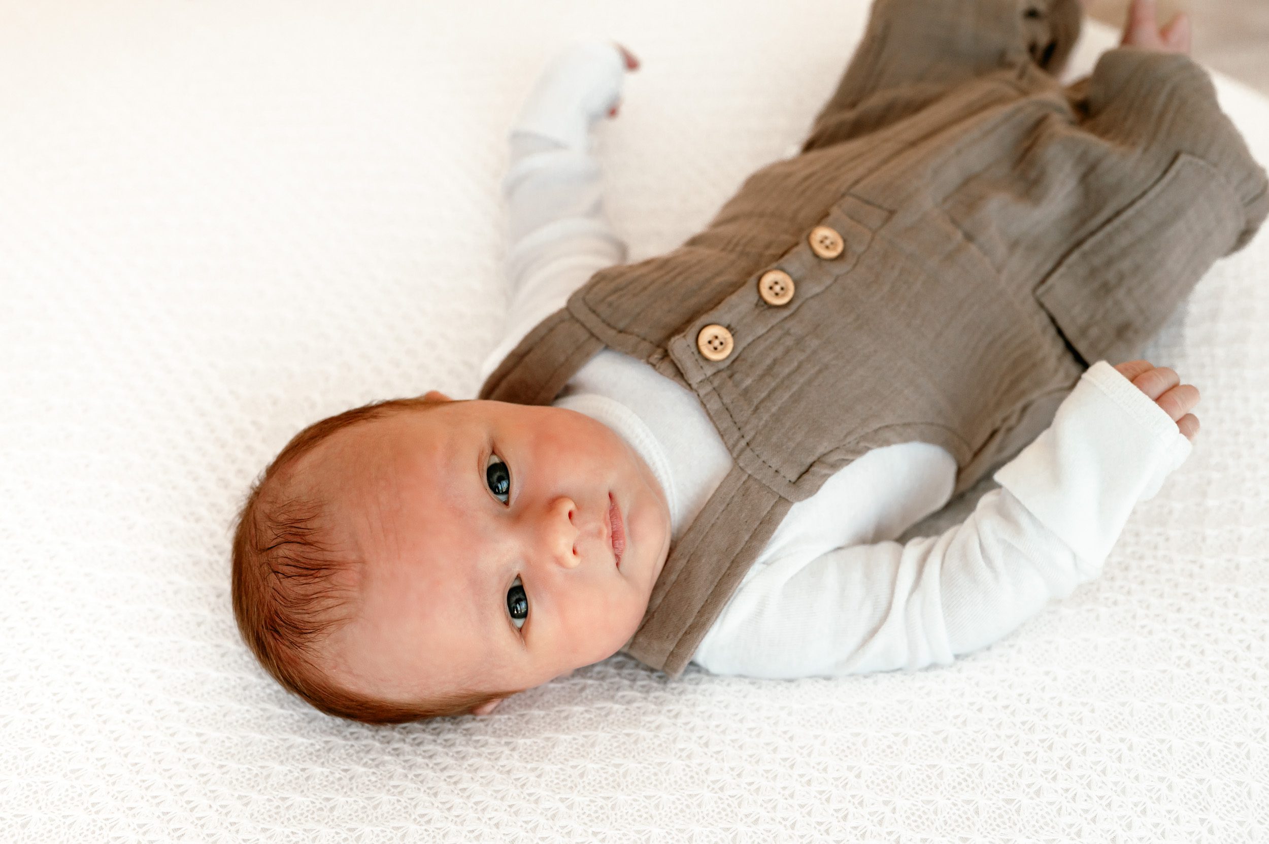 a baby boy laying on a white bean bag and looking back over his head toward the camera during a natural light newborn photoshoot