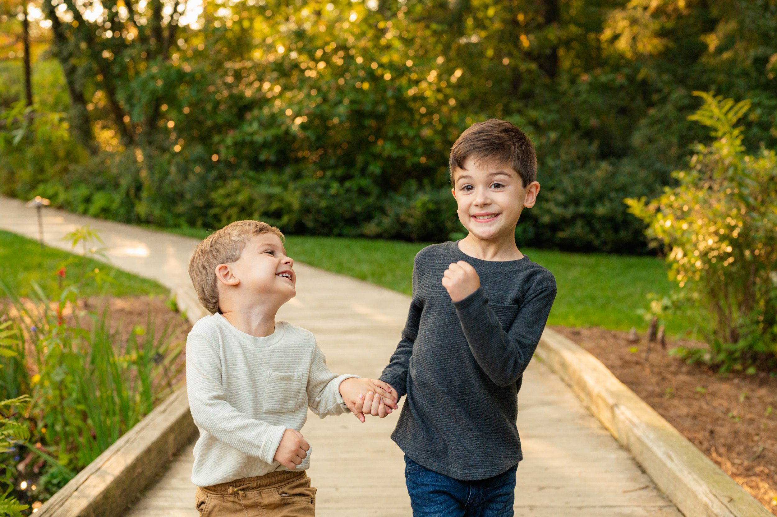 two young brothers holding hands and laughing as they march across a bridge during a West Chester family photoshoot