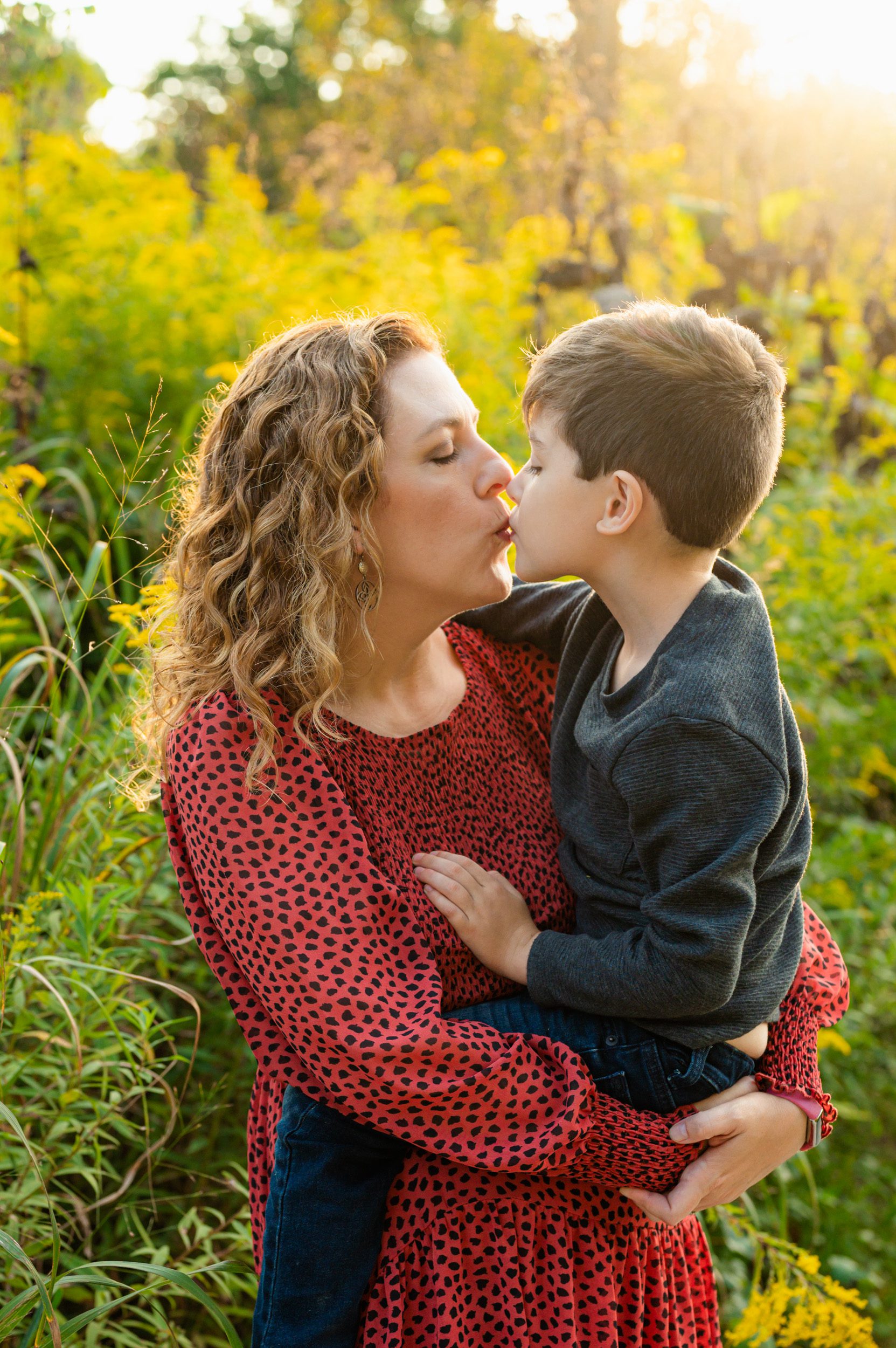 a mom standing in a field of yellow wildflowers and holding her young son in her arms as they kiss each other during a West Chester family photo session
