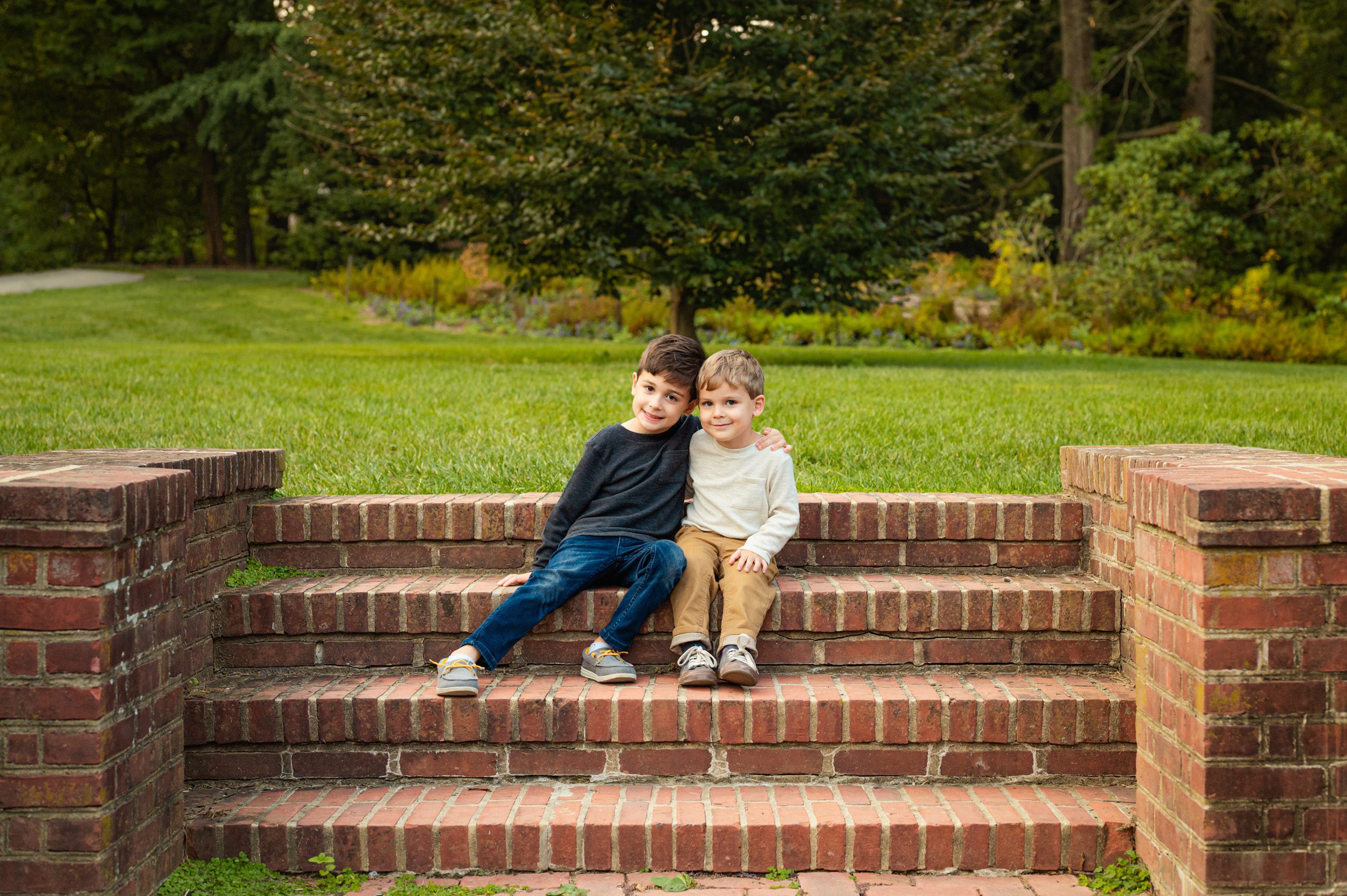 two young brothers sitting on brick steps with their arms around each other and smiling at the camera during a Longwood Gardens family photoshoot