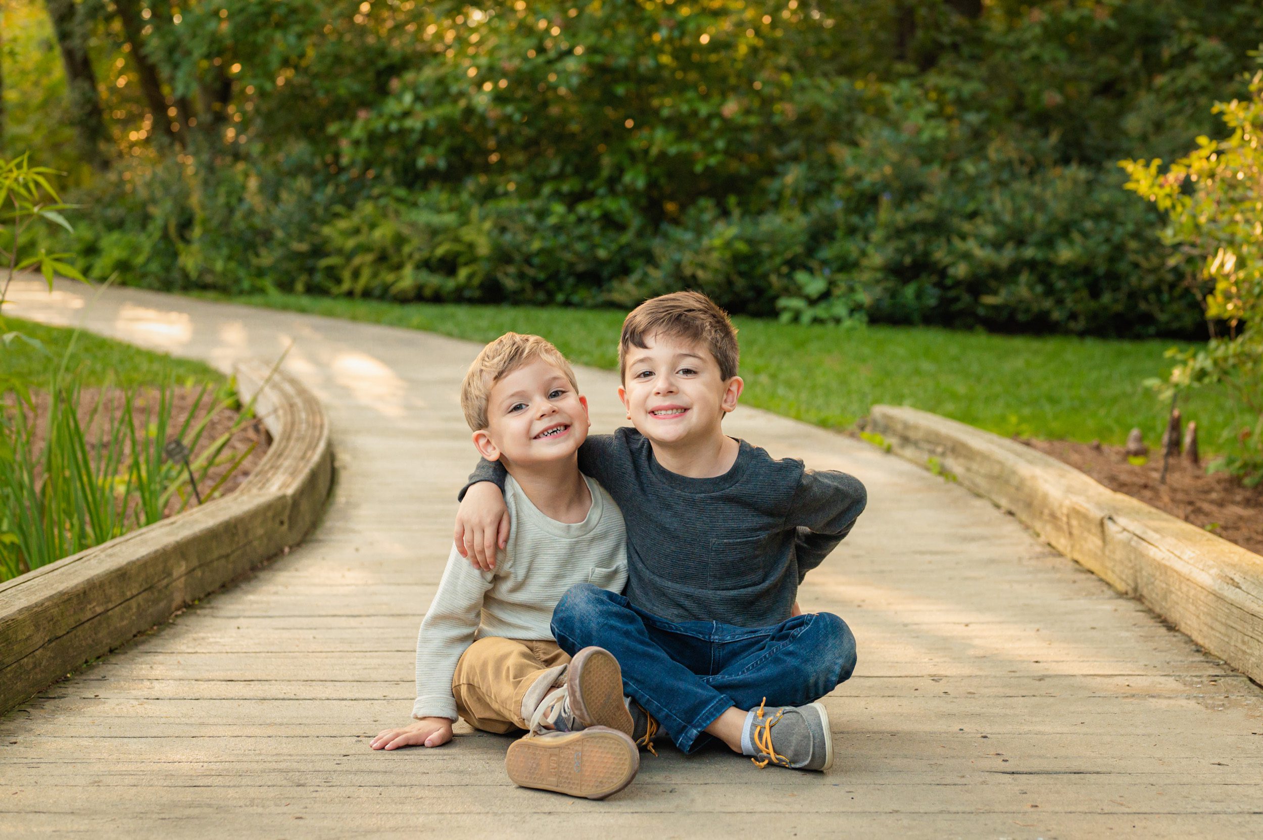 two young brothers sitting on a bridge with their arms around each other and smiling at the camera during a West Chester family photo session