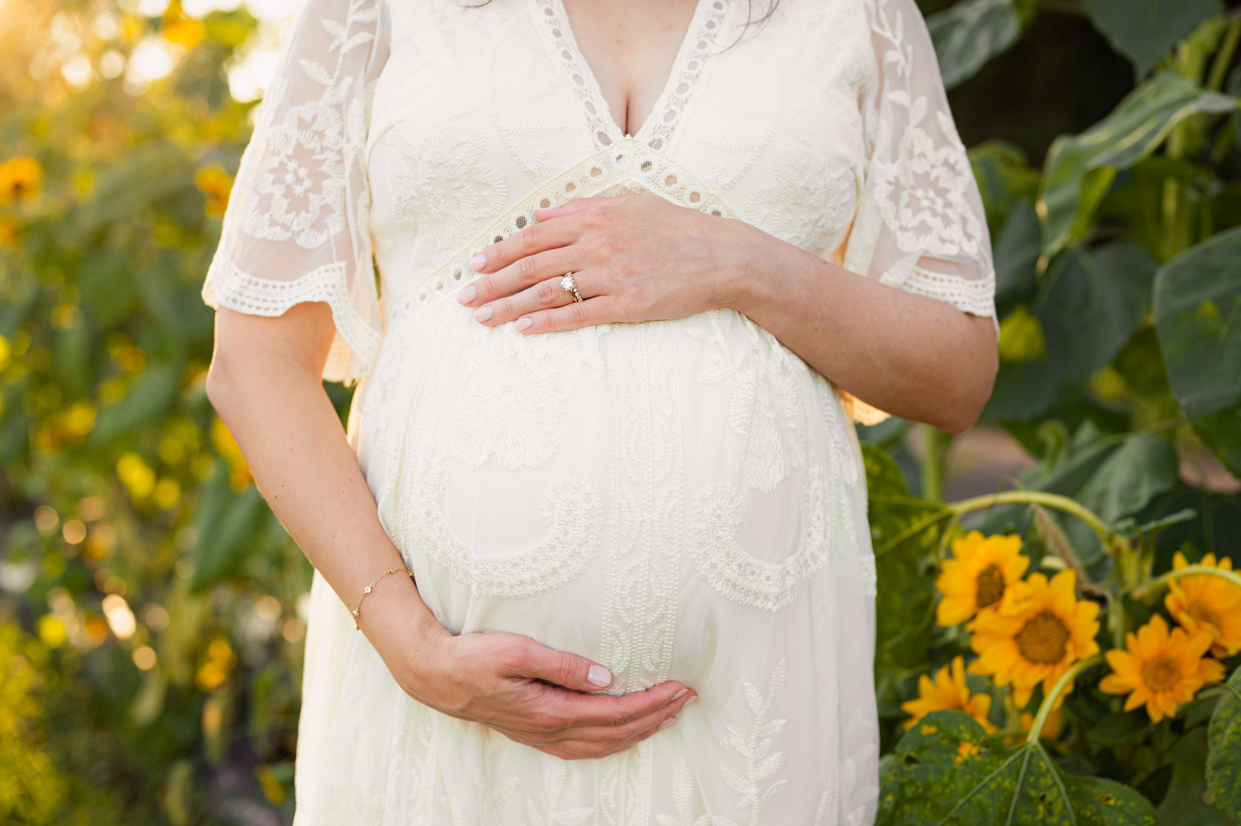 a close up shot of an expecting mom's belly while she stands in front of field of sunflowers in bloom during a Philadelphia maternity photo session