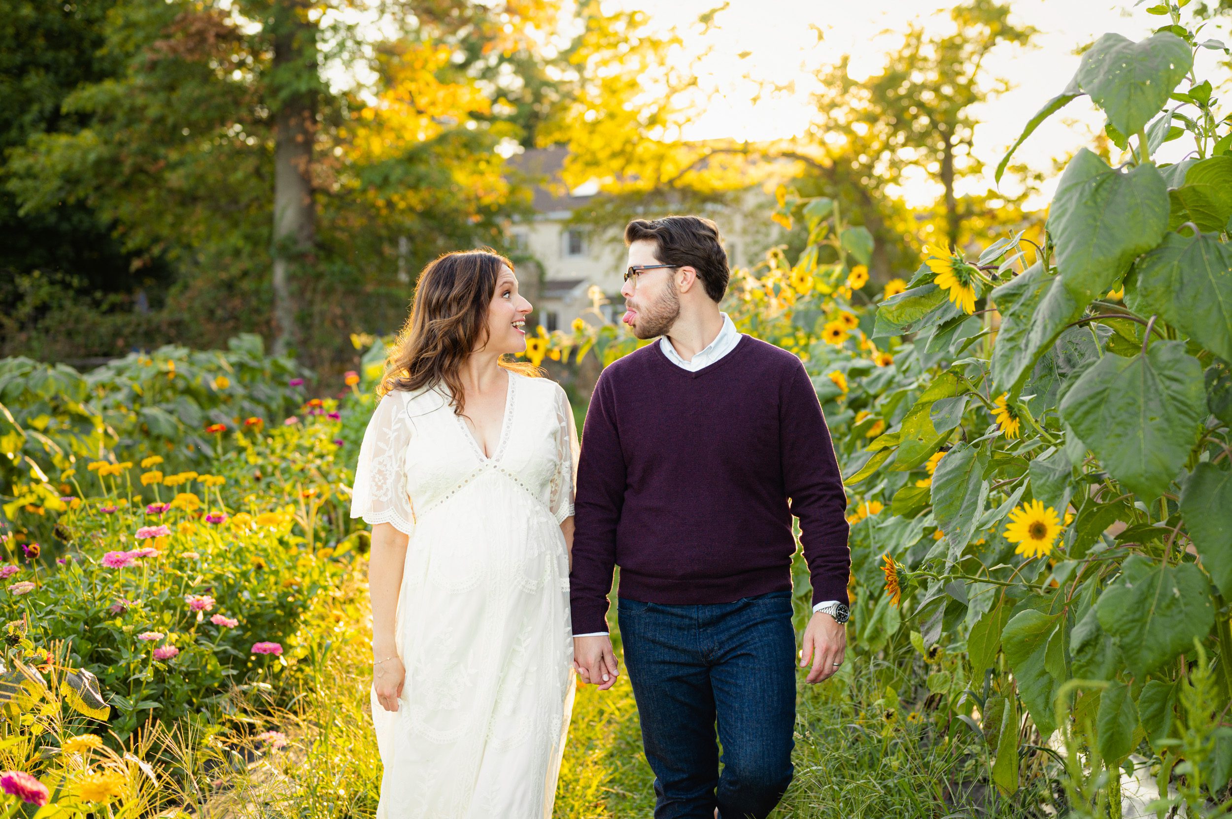 an expecting couple walking through a field of sunflowers and wildflowers while they make silly faces at each other during a maternity photoshoot