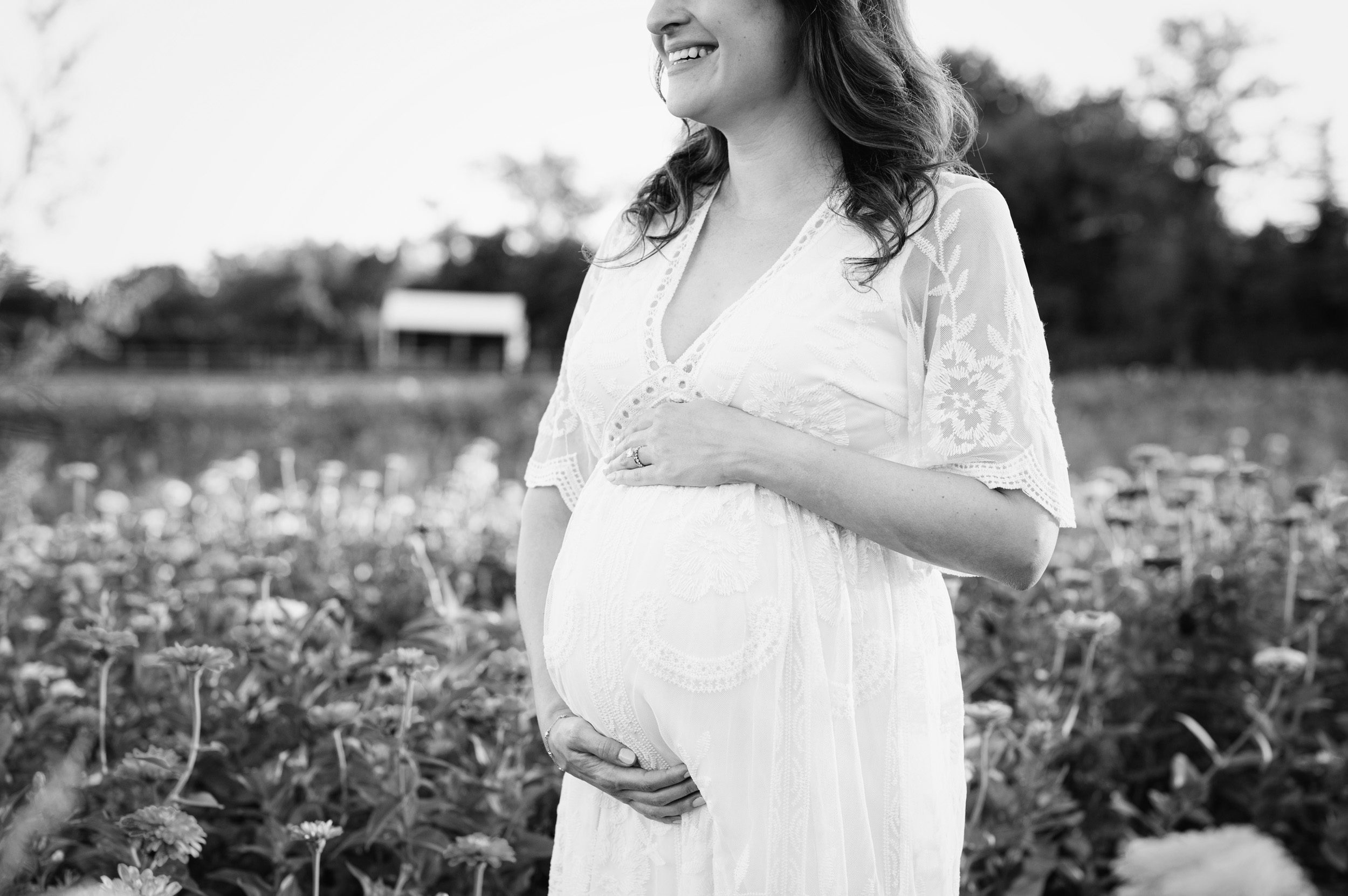a black and white close up of an expecting mom in a white dress smiling as she cradles her belly during a Philadelphia maternity photoshoot