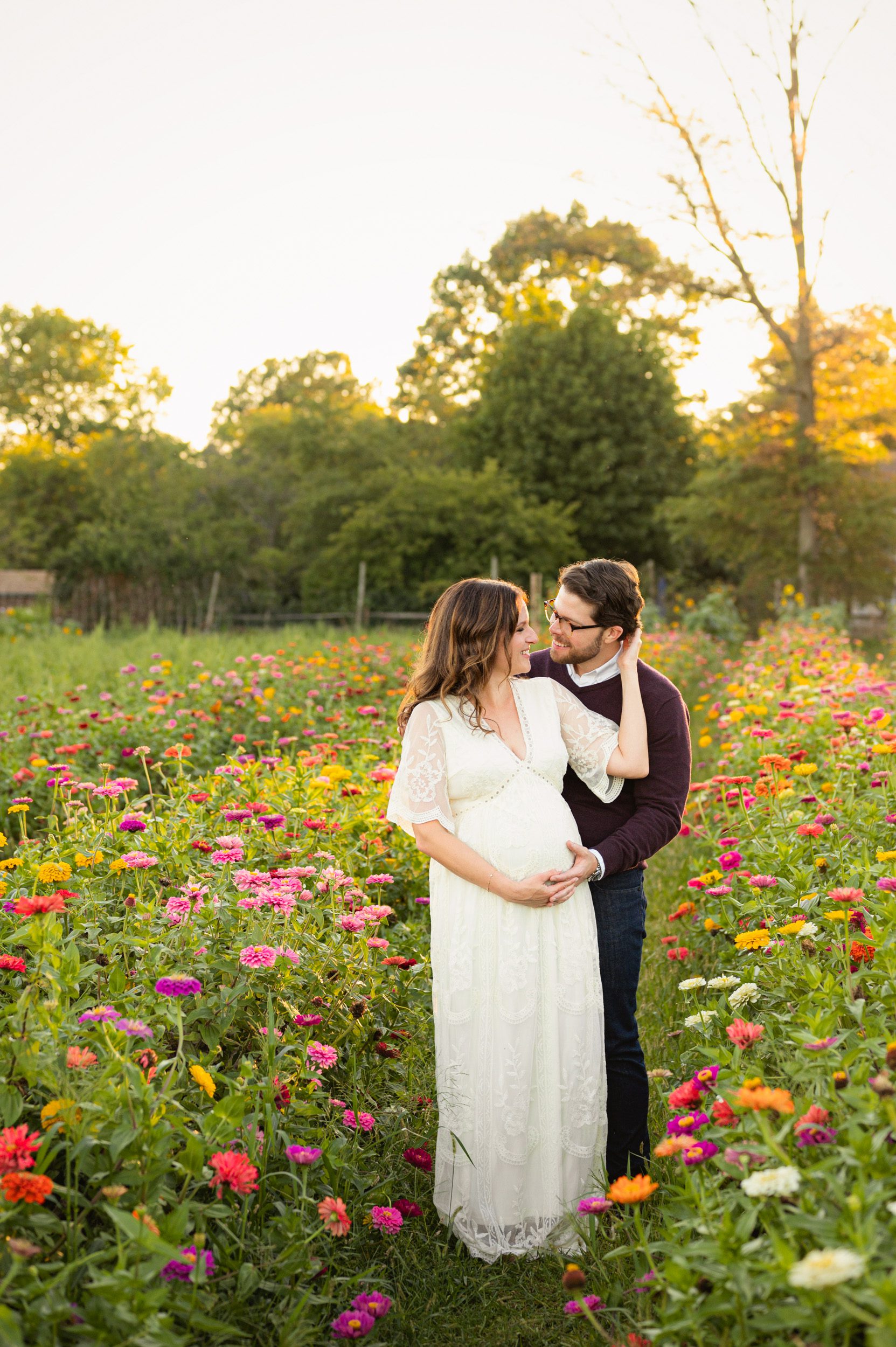 an expecting couple standing in a field of wildflowers and smiling at each other during a Philadelphia maternity photoshoot