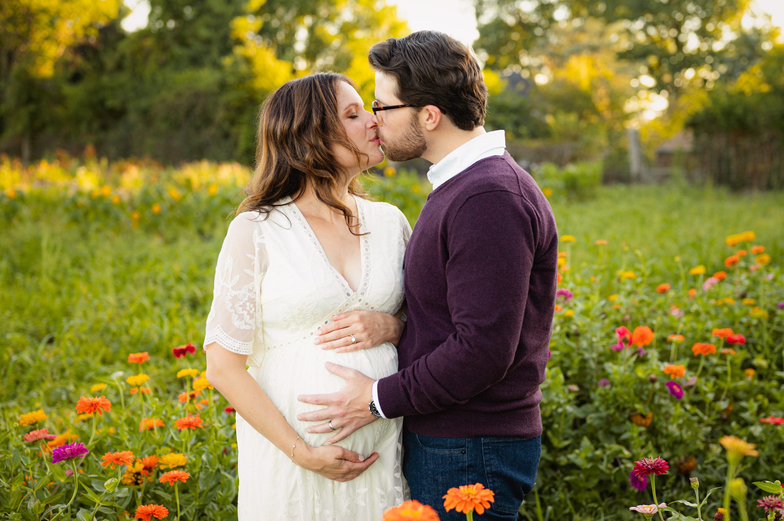 an expecting couple standing in a field of wildflowers and kissing while they both hold mom's belly during a maternity photoshoot