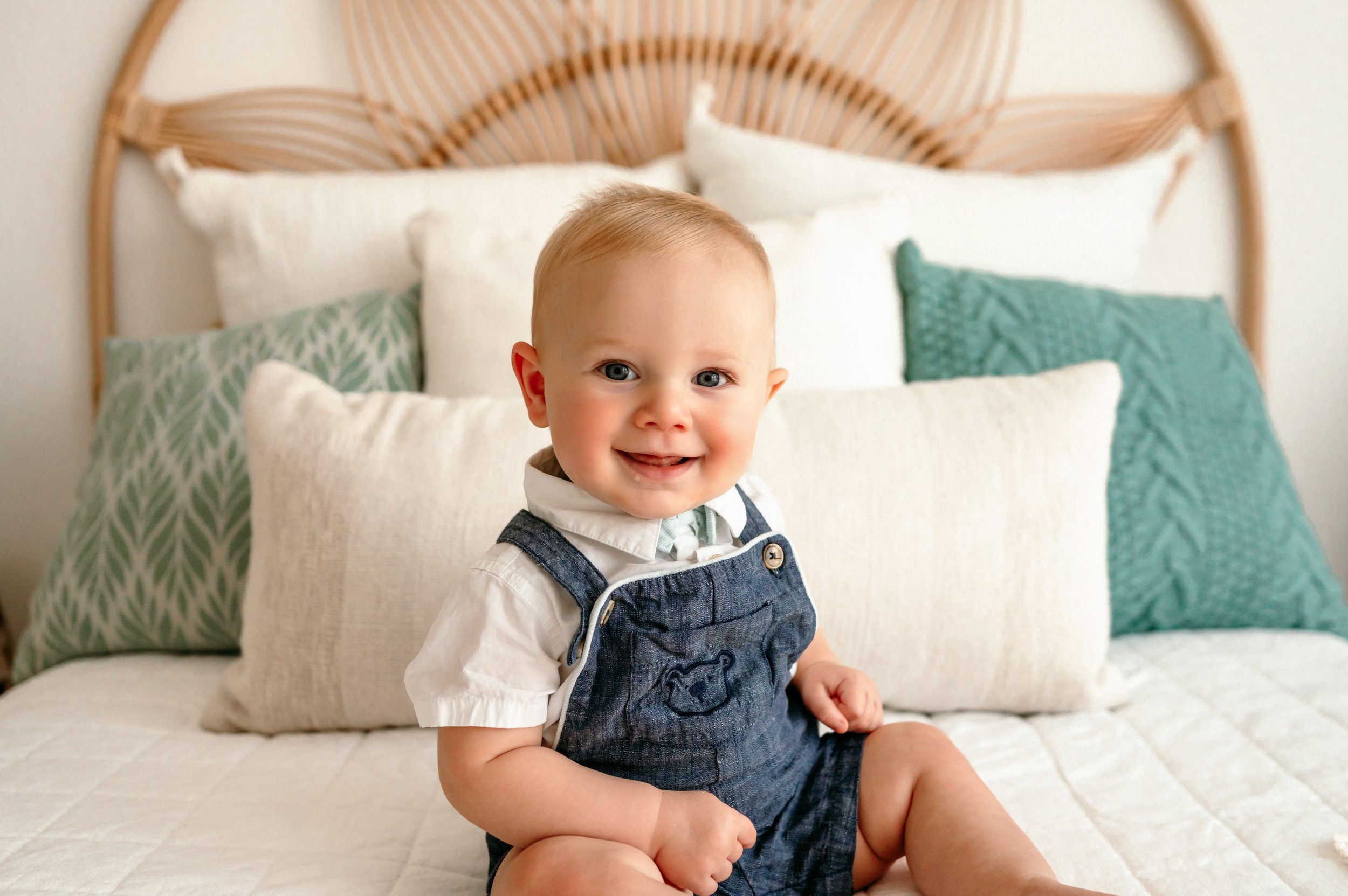 a baby boy sitting in a bed and smiling at the camera during a baby milestone session