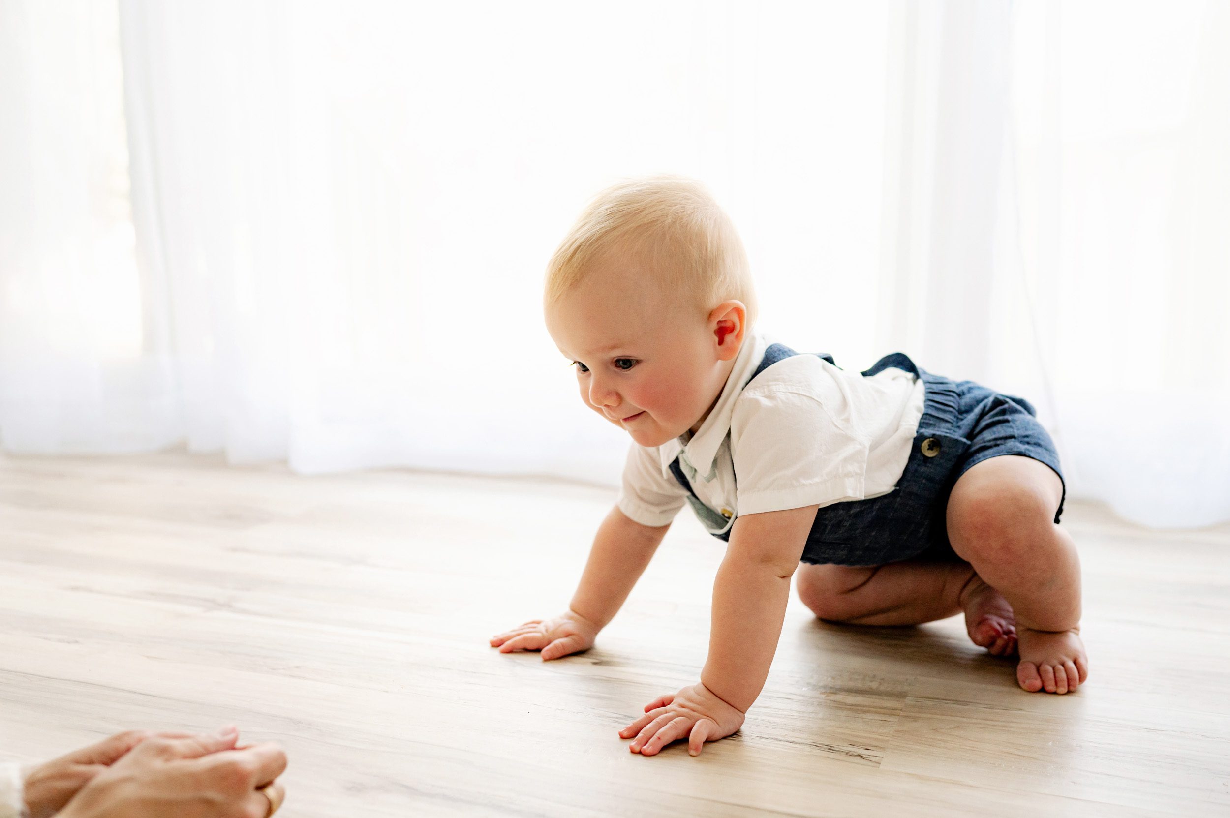 a backlit picture of a baby boy crawling across the floor toward his mom's arms during a milestone photoshoot