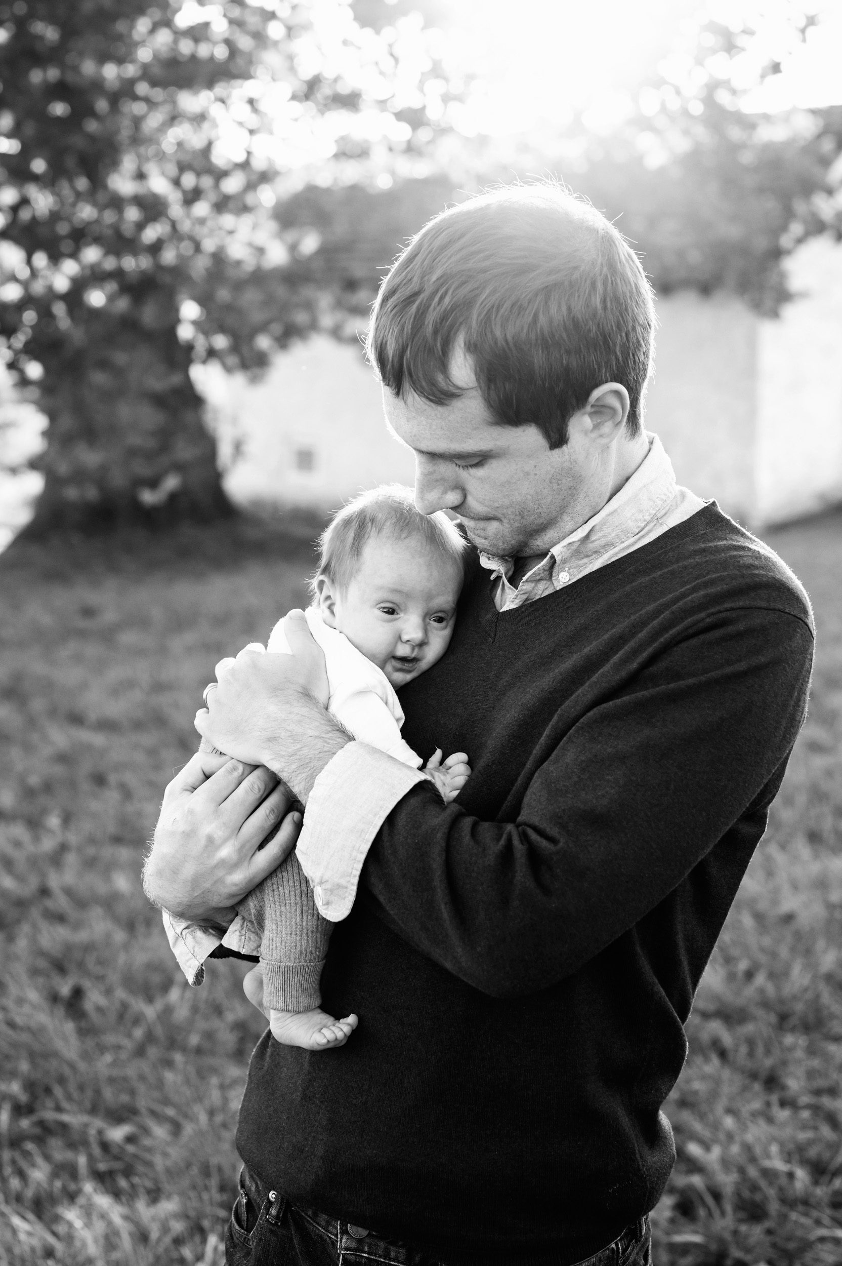 a black and white picture of a dad holding his baby boy against his chest during a King of Prussia family photo session
