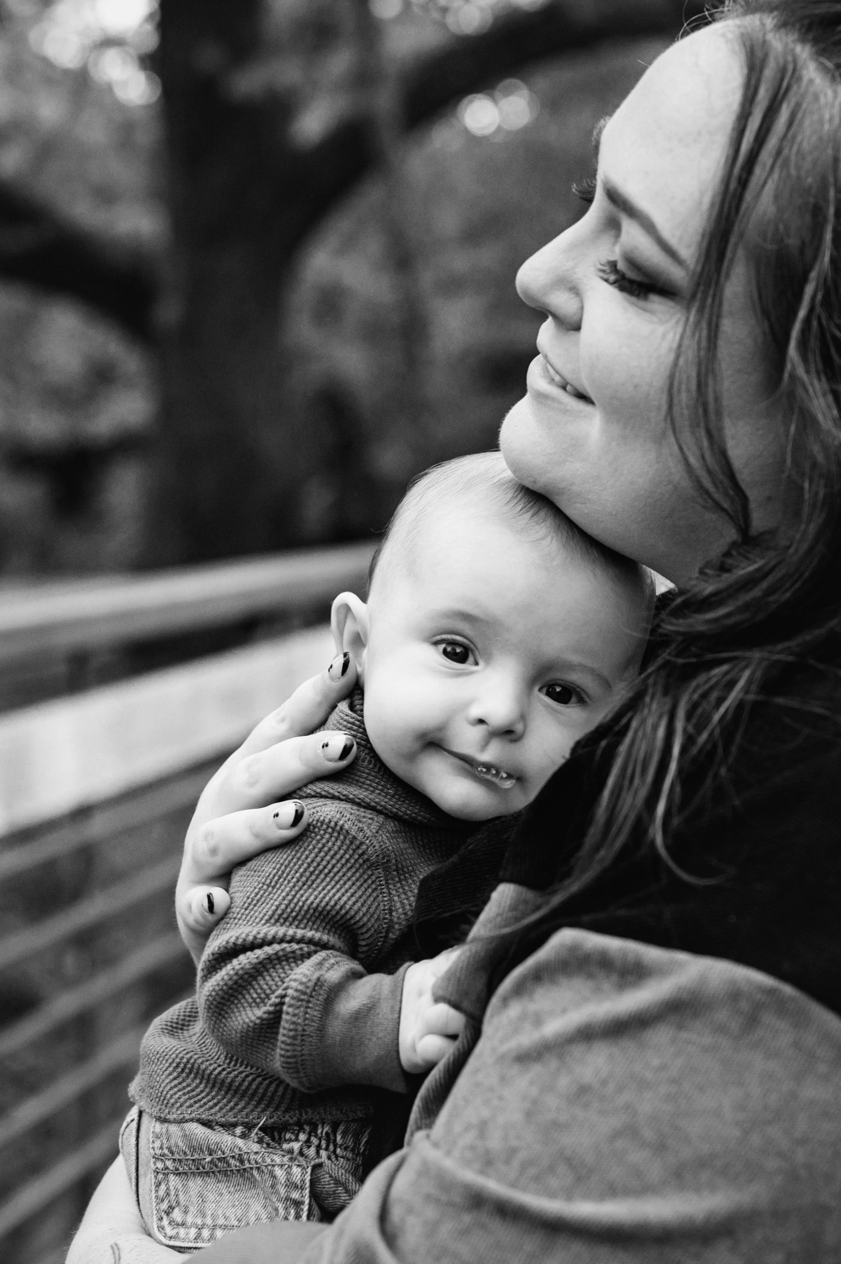 black and white picture of a baby boy snuggled up against his mom's chest as he looks at the camera and blows spit bubbles during a family photoshoot