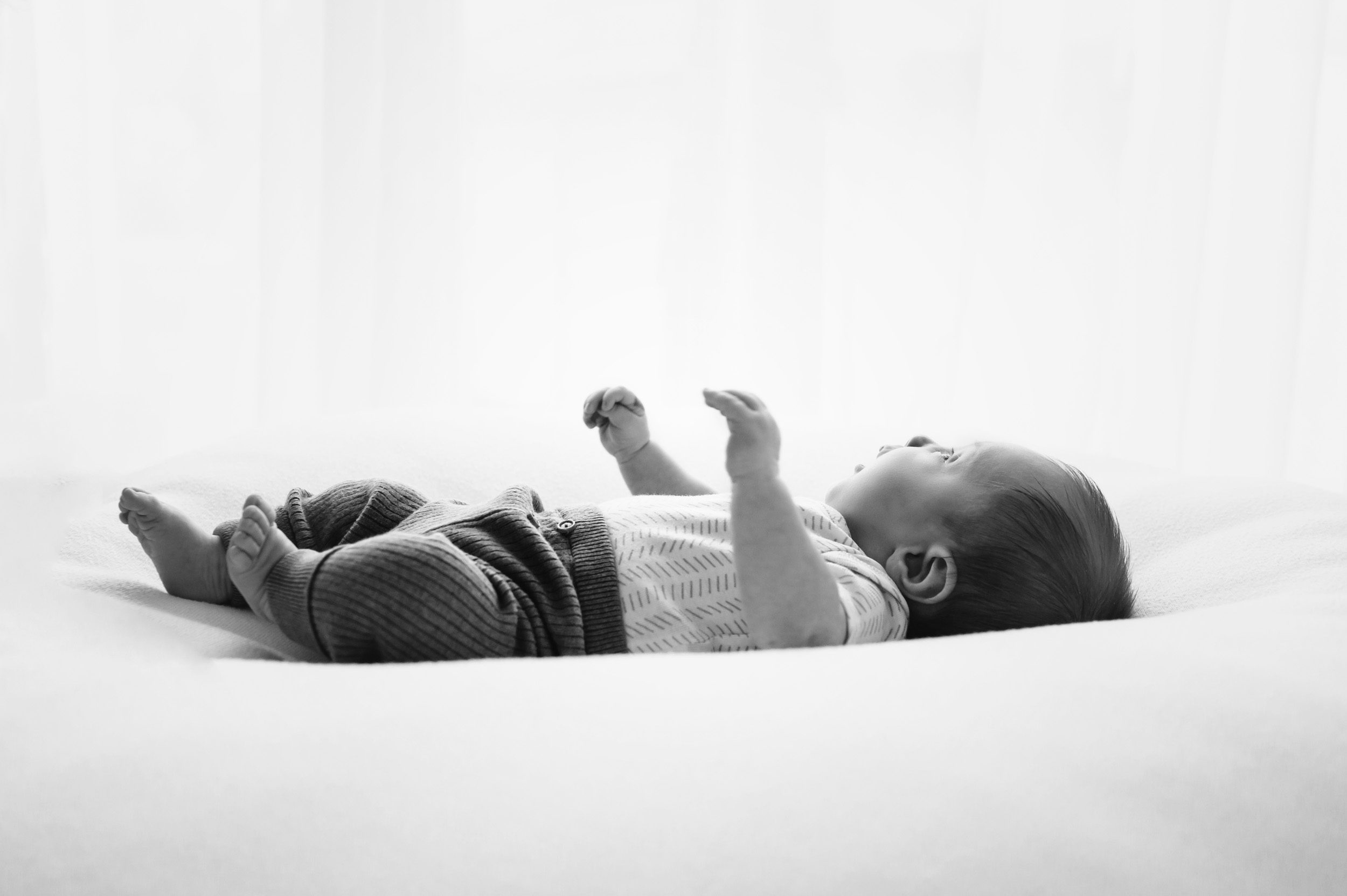 a black and white backlit profile picture of a baby boy laying on a white bean bag during a newborn photo session