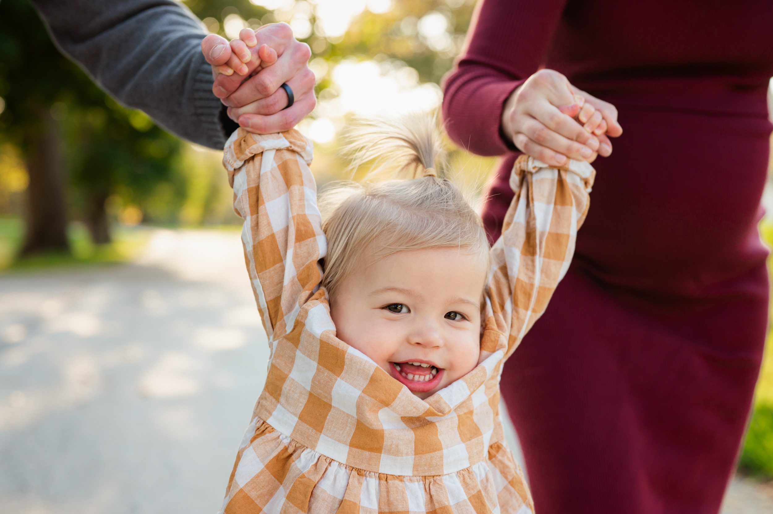 a close up picture of a young girl smiling at the camera as her parents hold her hands and swing her up in the air during a maternity photo session