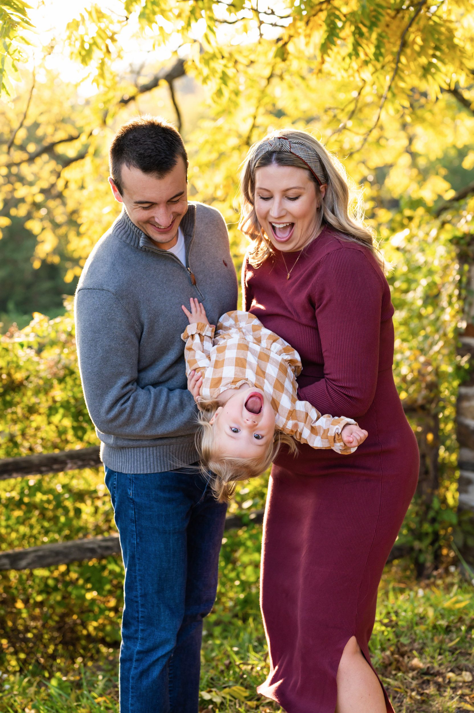 expecting parents holding their young daughter upside down and laughing as they look down at her during a maternity photoshoot