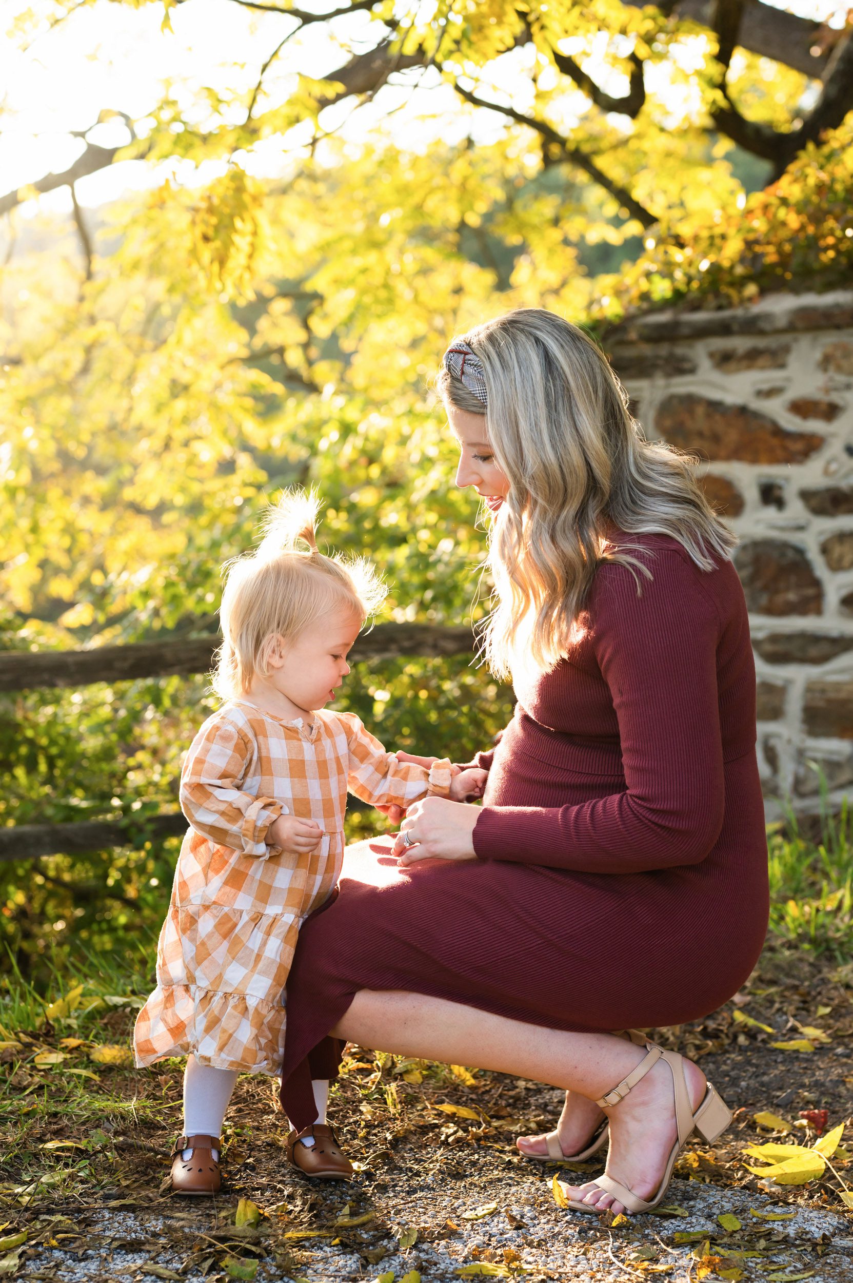 an expecting mother kneeling down as her young daughter reaches out to touch her belly during a maternity photoshoot