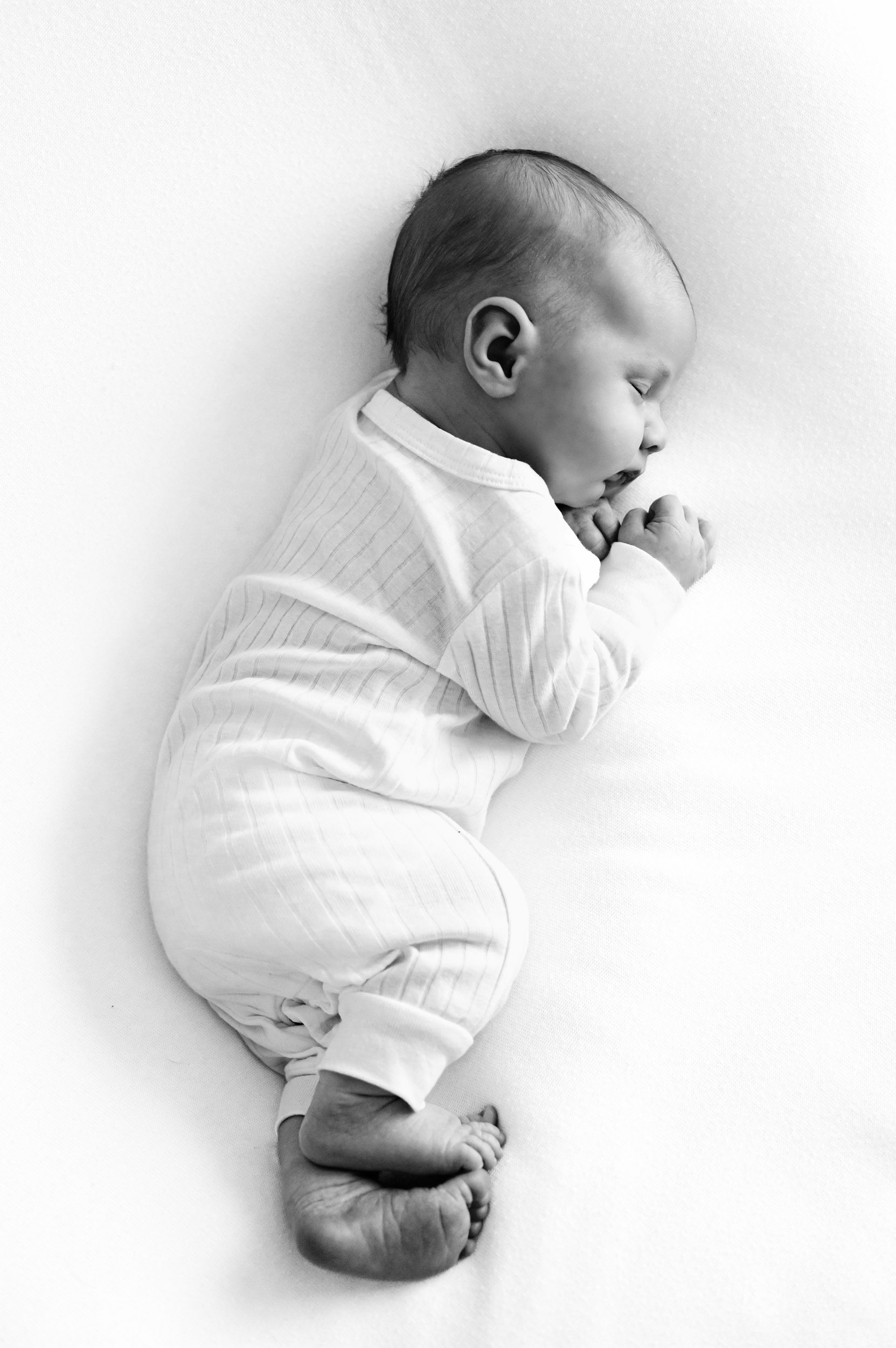 a black and white picture of a newborn baby laying on his side with his feet and hands curled up close t his body during a newborn baby photoshoot