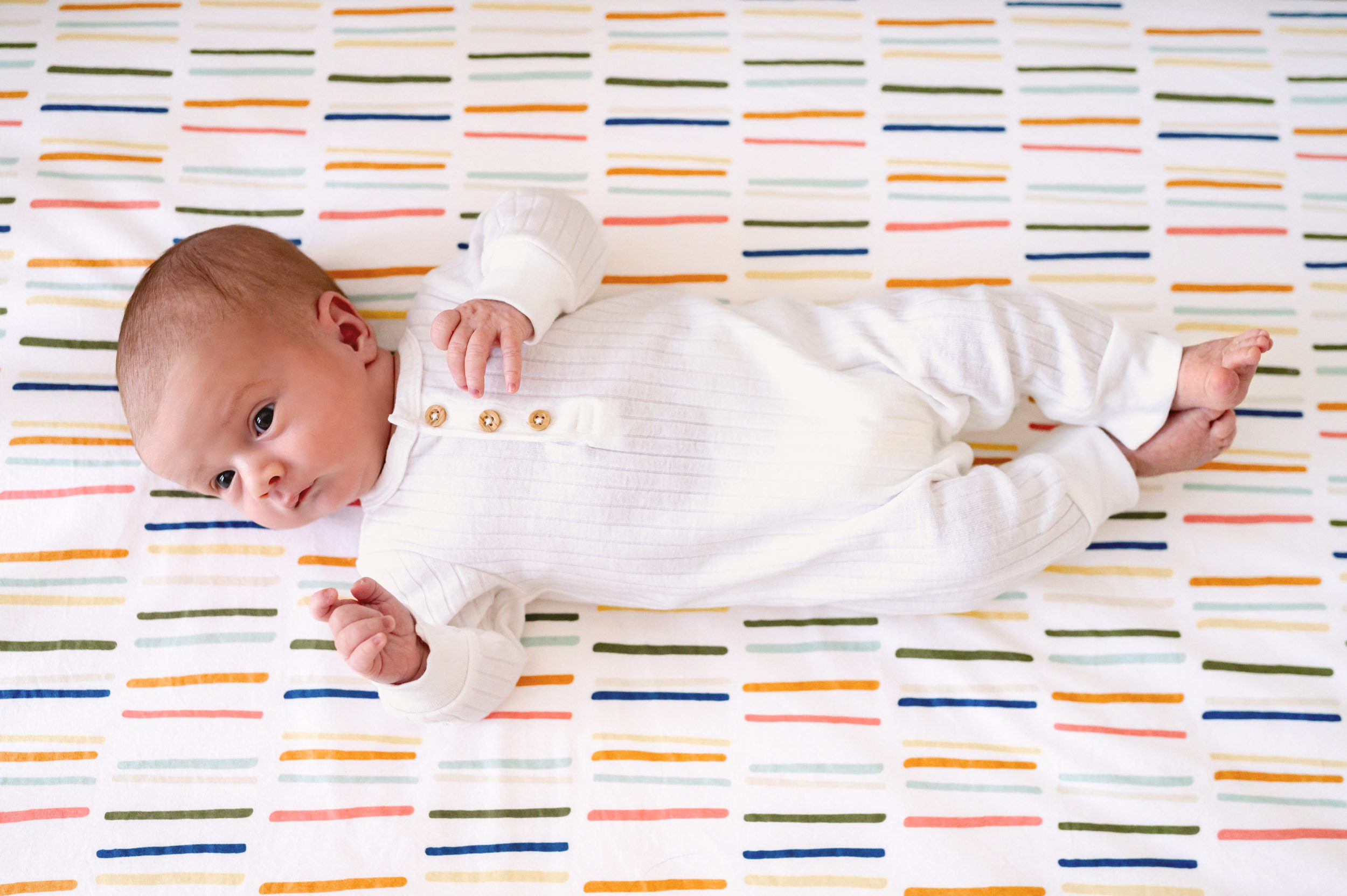 a baby boy laying on his back on a colorfully striped crib mattress 