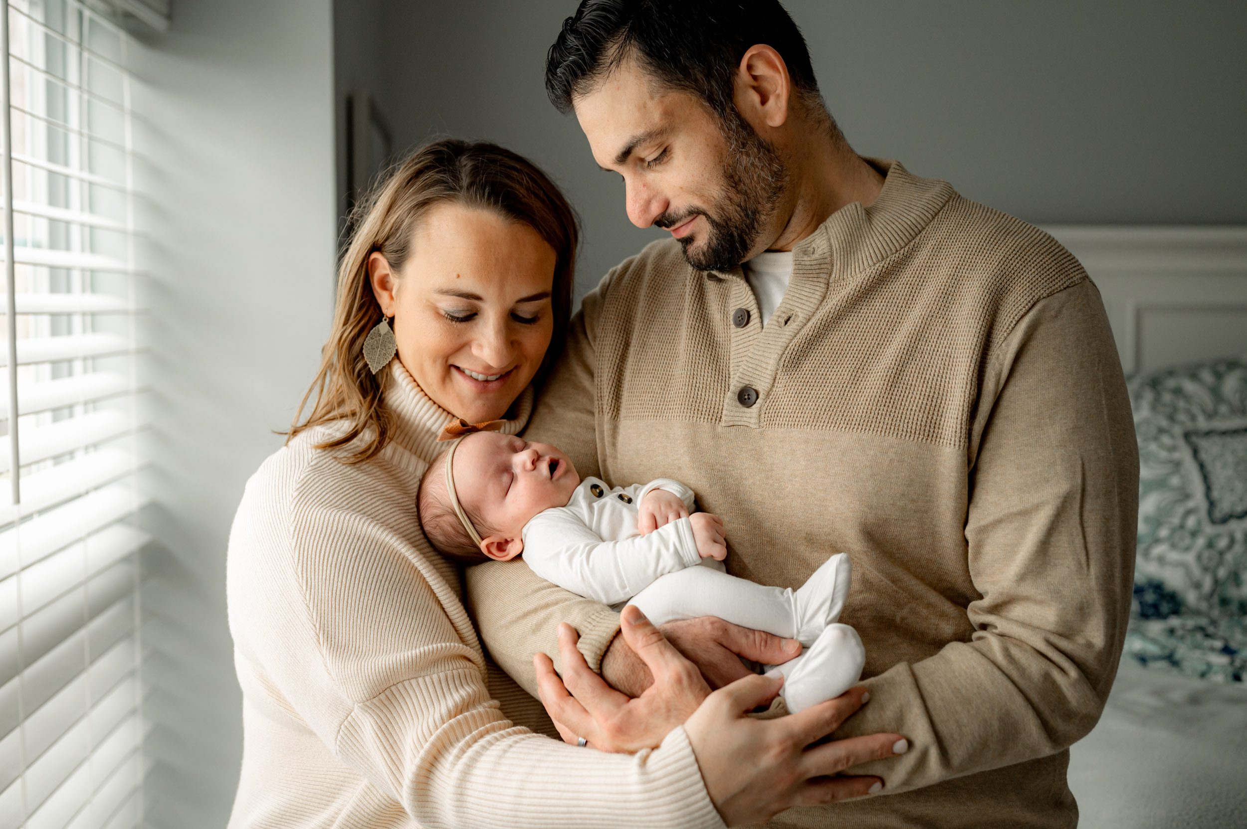 a baby girl girl cradled in her dad's arms as her parents smile down at her during a newborn photoshoot