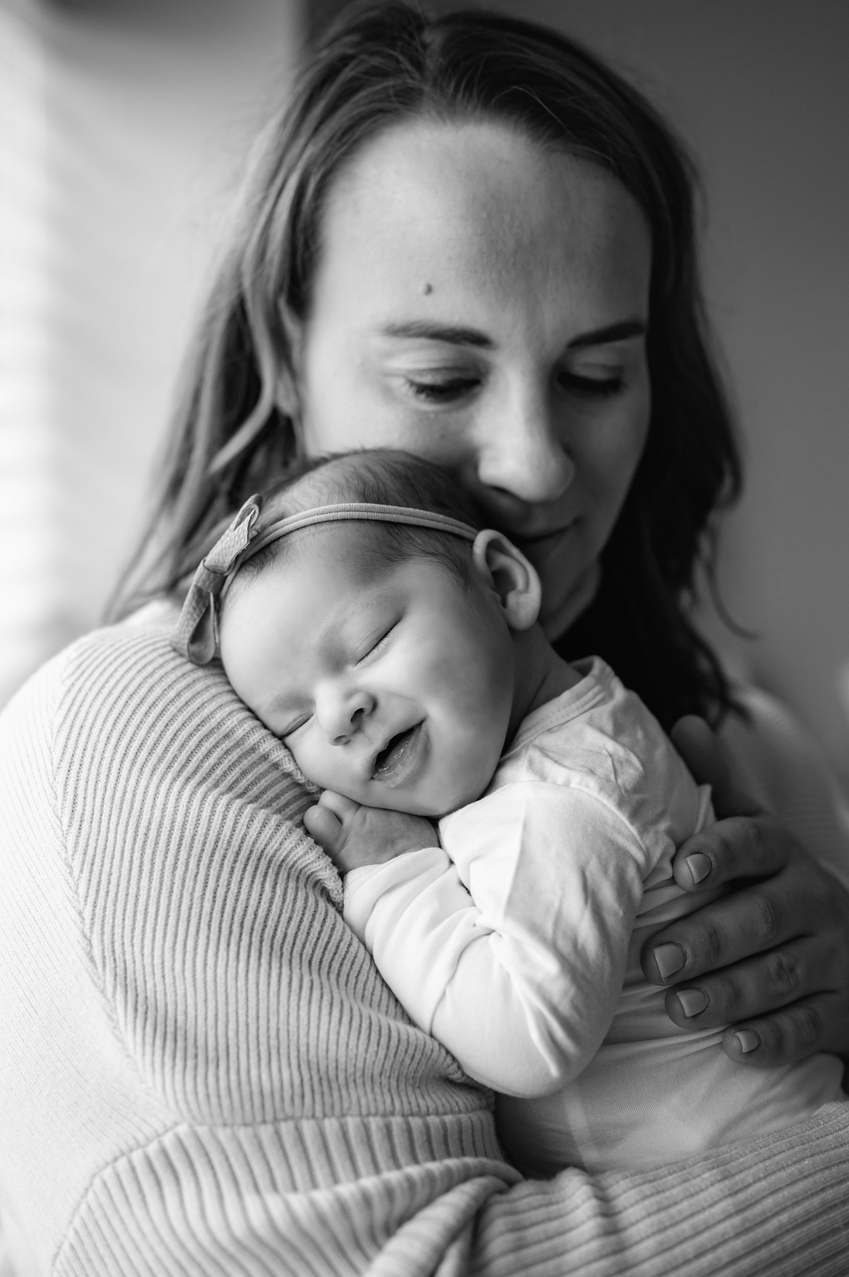 a black and white picture of a baby girl snuggled up against her mom's chest and smiling during a newborn photoshoot
