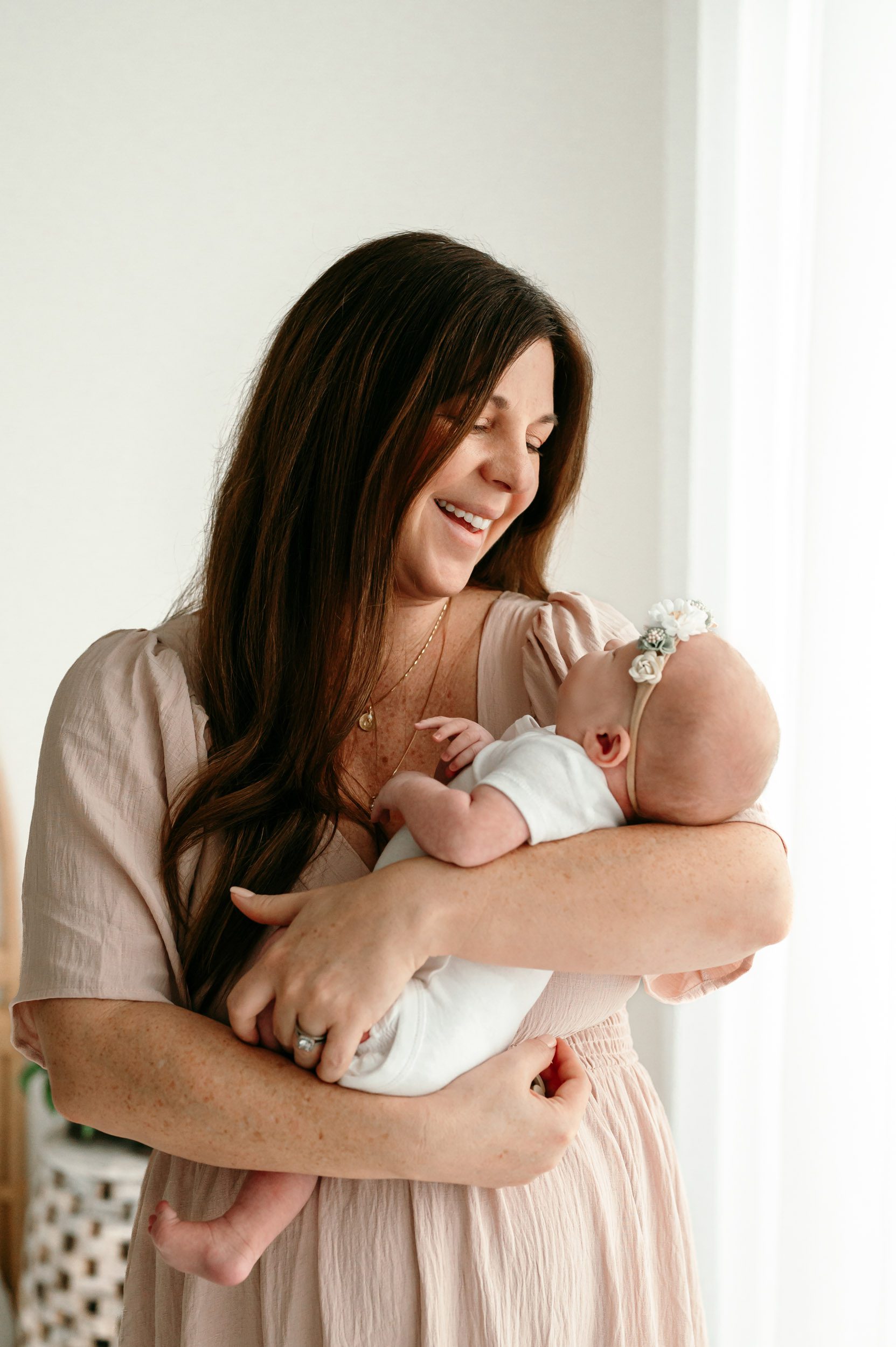 a mother cradling her baby girl in her arms and smiling down at her during a newborn photoshoot
