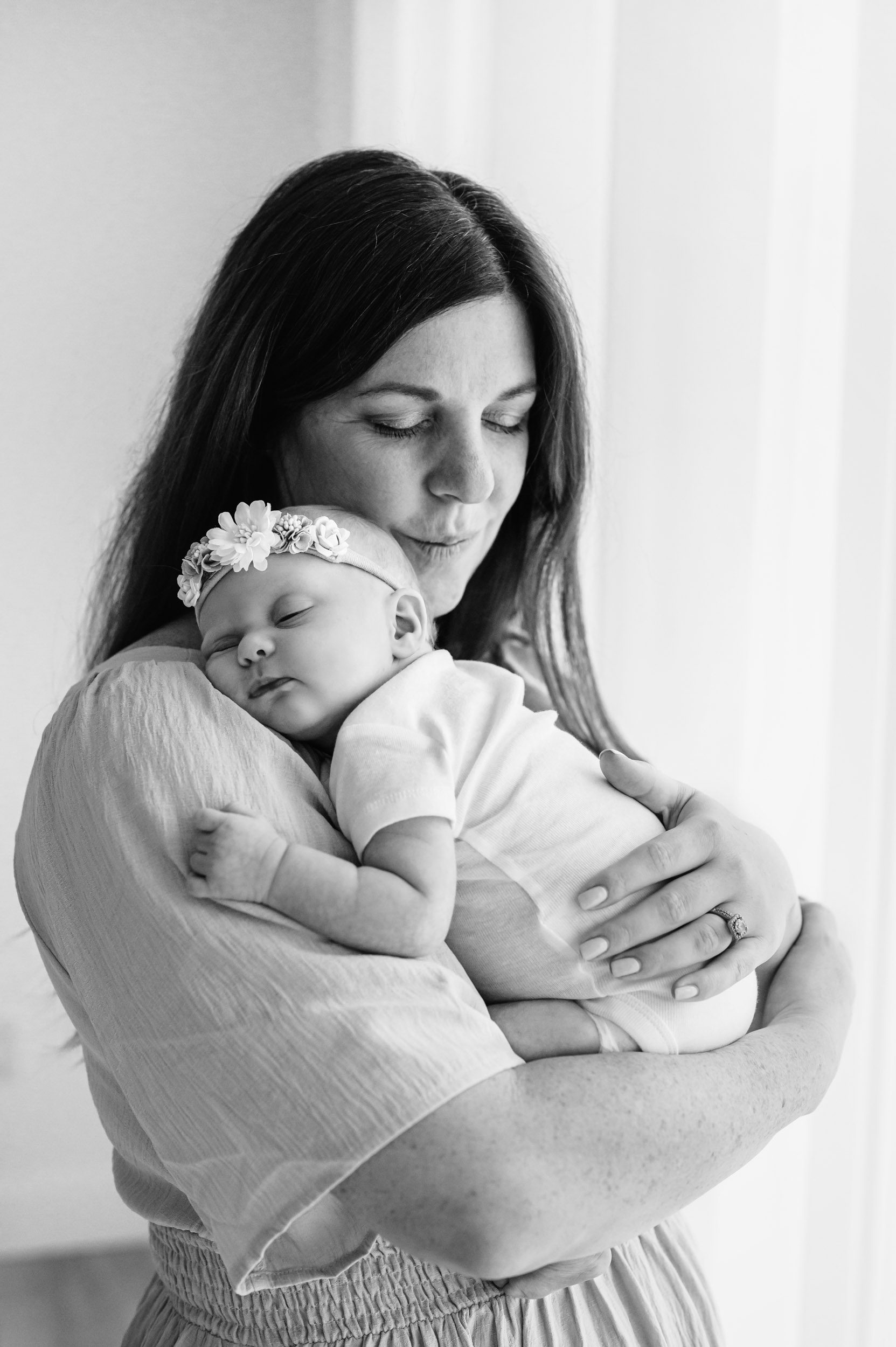 a black and white picture of a mom hugging her baby girl against her chest during a newborn photoshoot