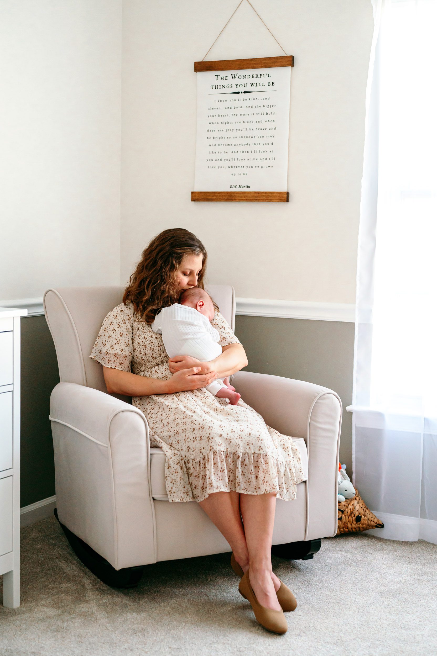 a mom sitting in a rocking chair holding her baby boy against her chest and kissing him on the head during a newborn baby photoshoot