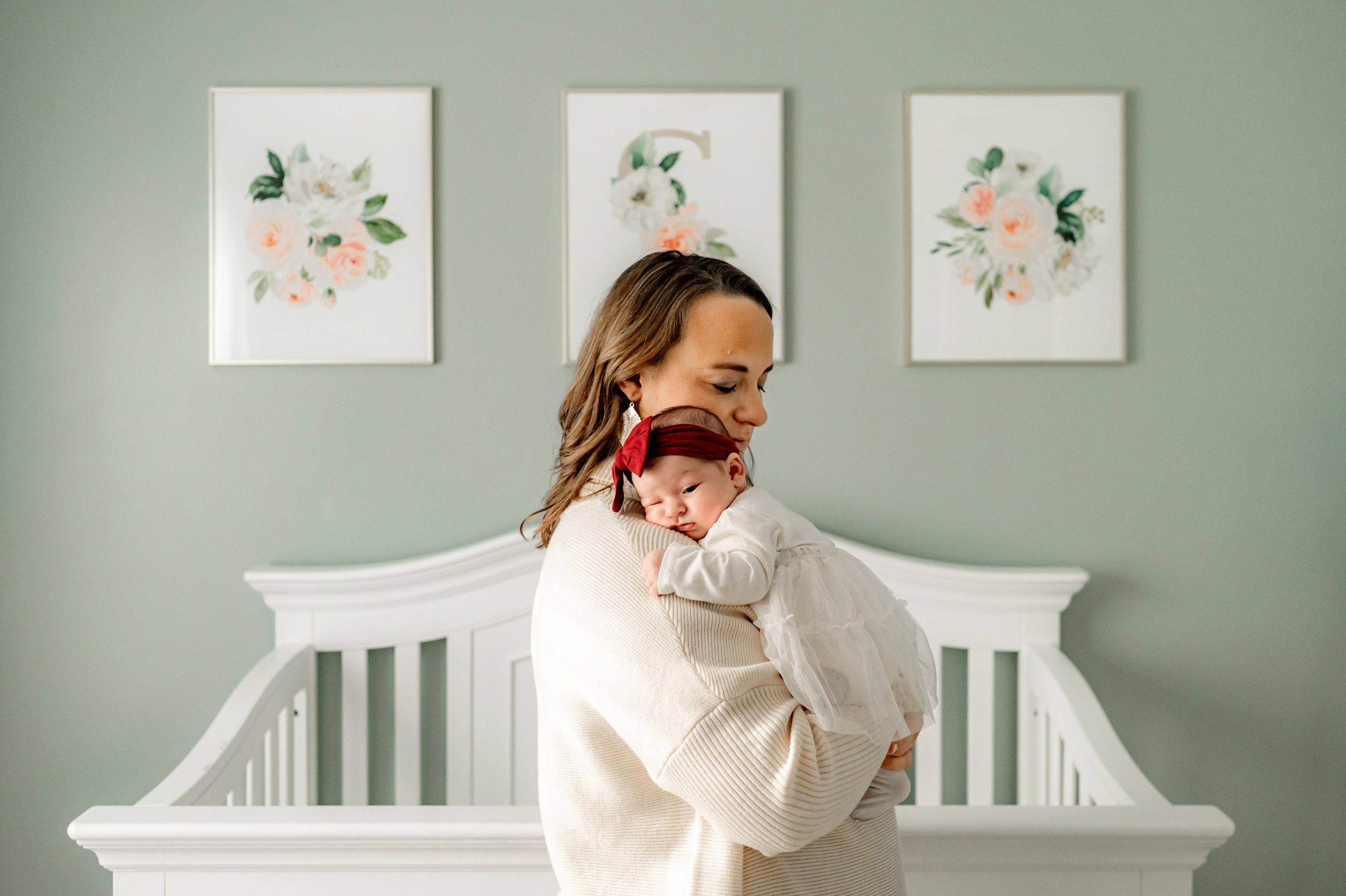 a mom standing in front of the crib in her daughter's nursery and cradling her baby girl against her chest during an in home newborn photography session