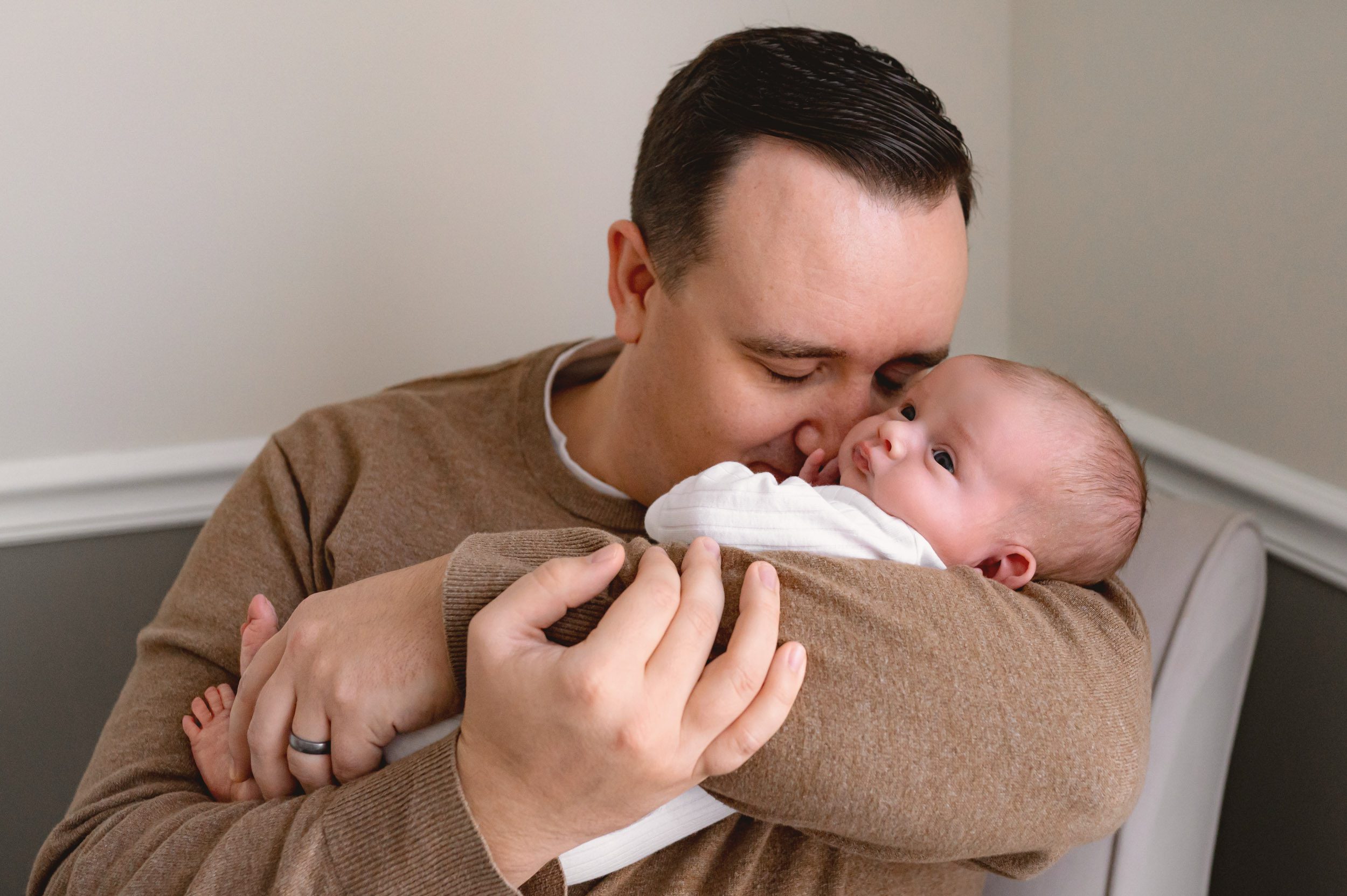 a dad cradling his newborn son in his arms and gently touching his nose to the baby's cheek during a newborn baby photography session