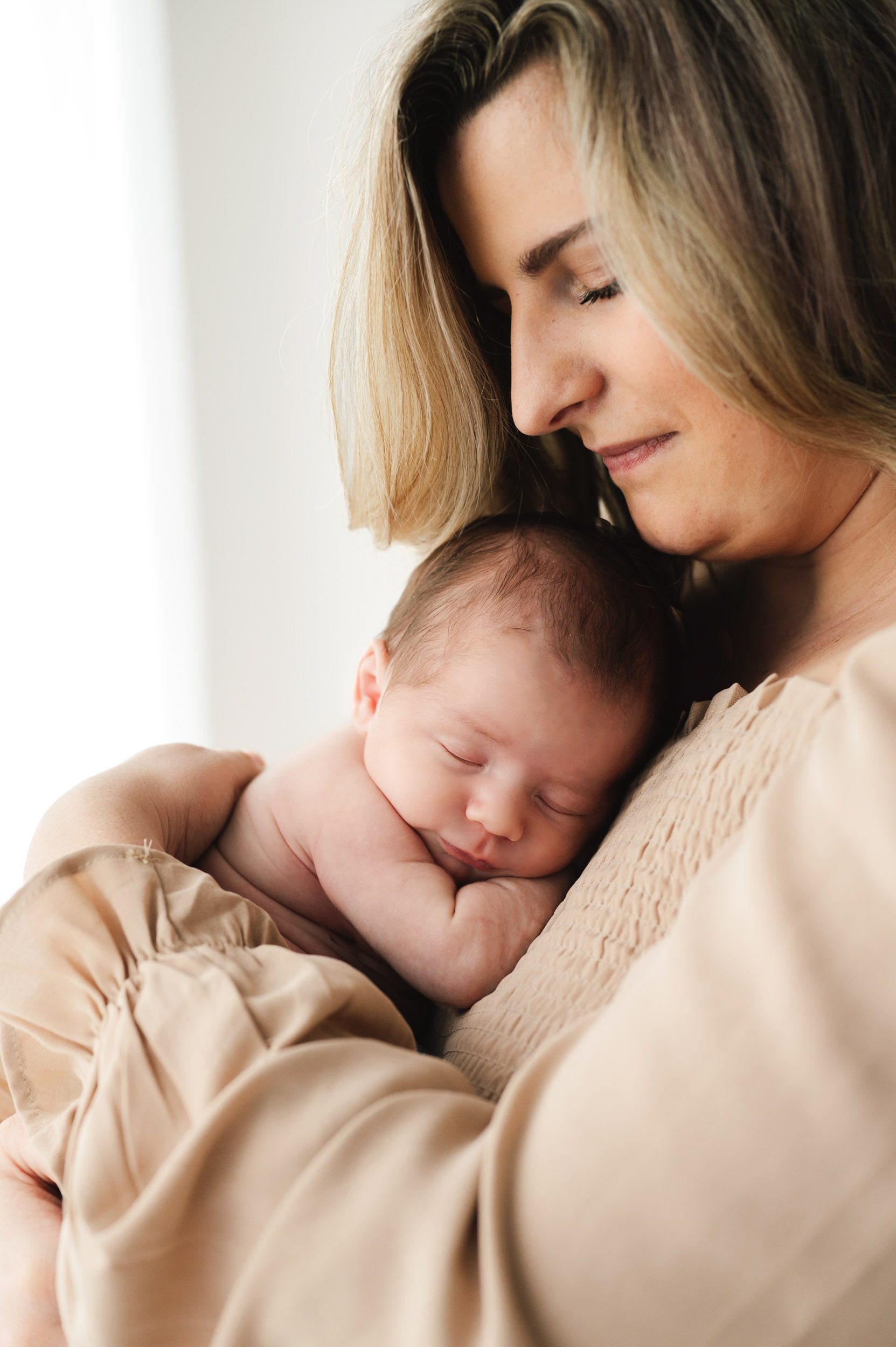 a new mom holding her baby boy against her chest and smiling down at him during a newborn lifestyle photography session