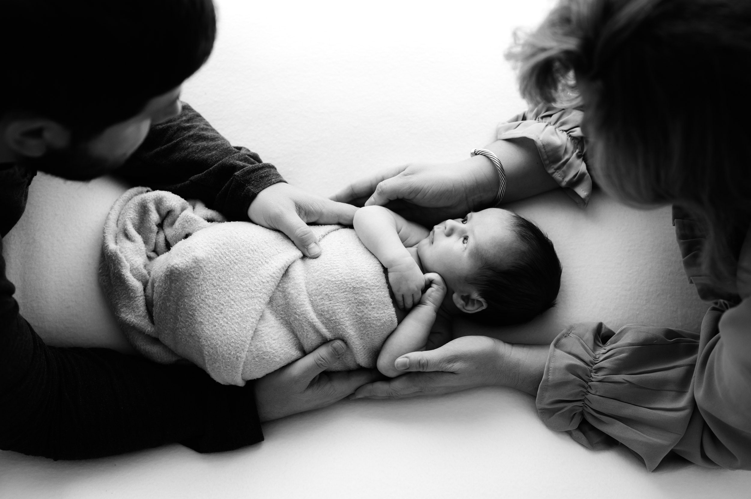 a black and white picture of a baby boy taken from above with his parents cradling him