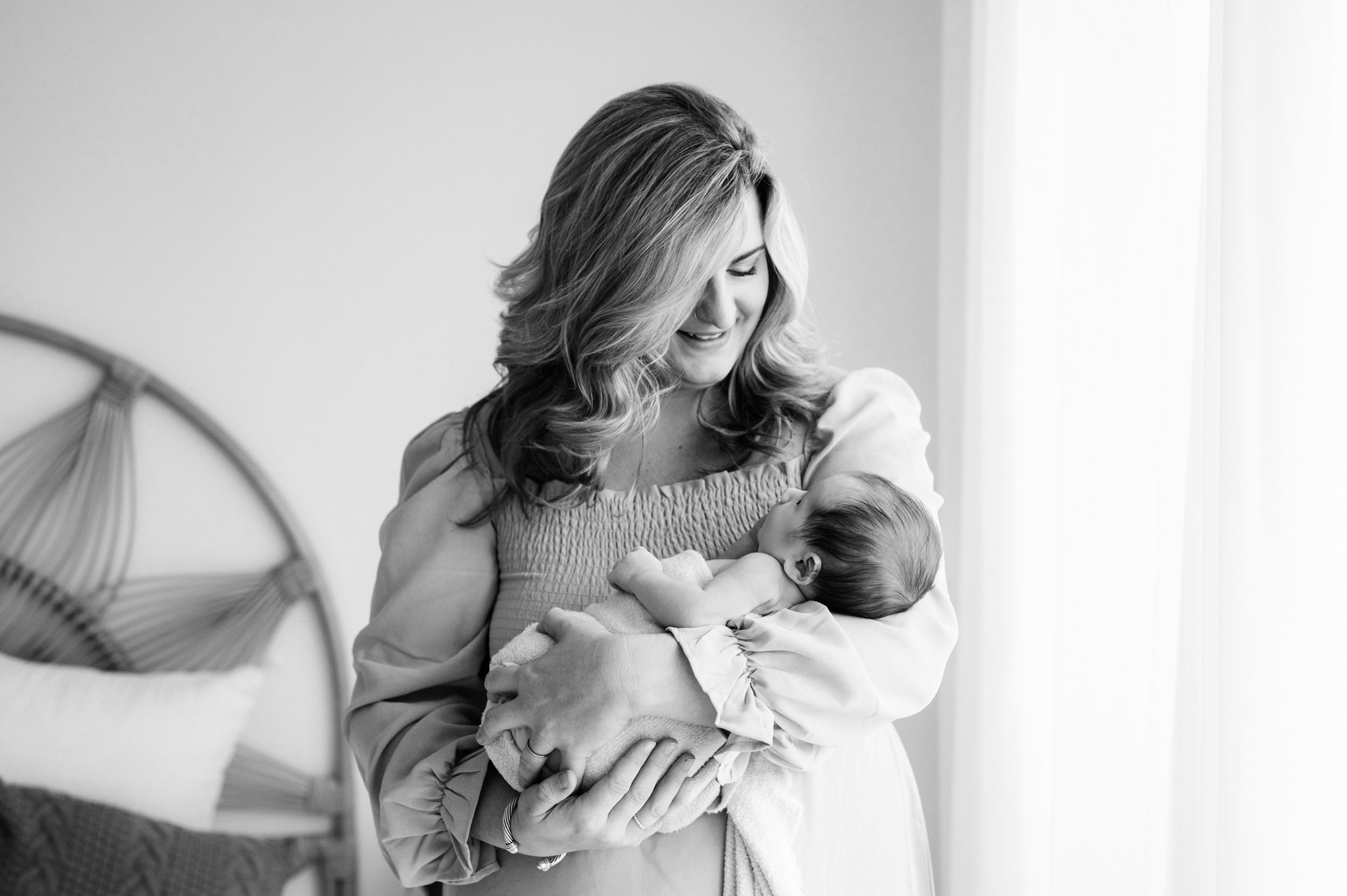 a black and white picture of a new mother cradling her baby boy in her arms and smiling down at him during a newborn photoshoot