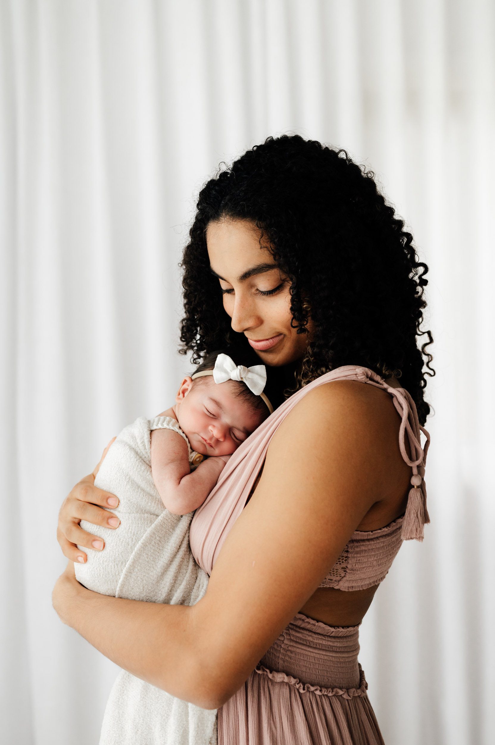 a new mom holding her baby girl against her chest and smiling down at her during a natural light newborn photo session