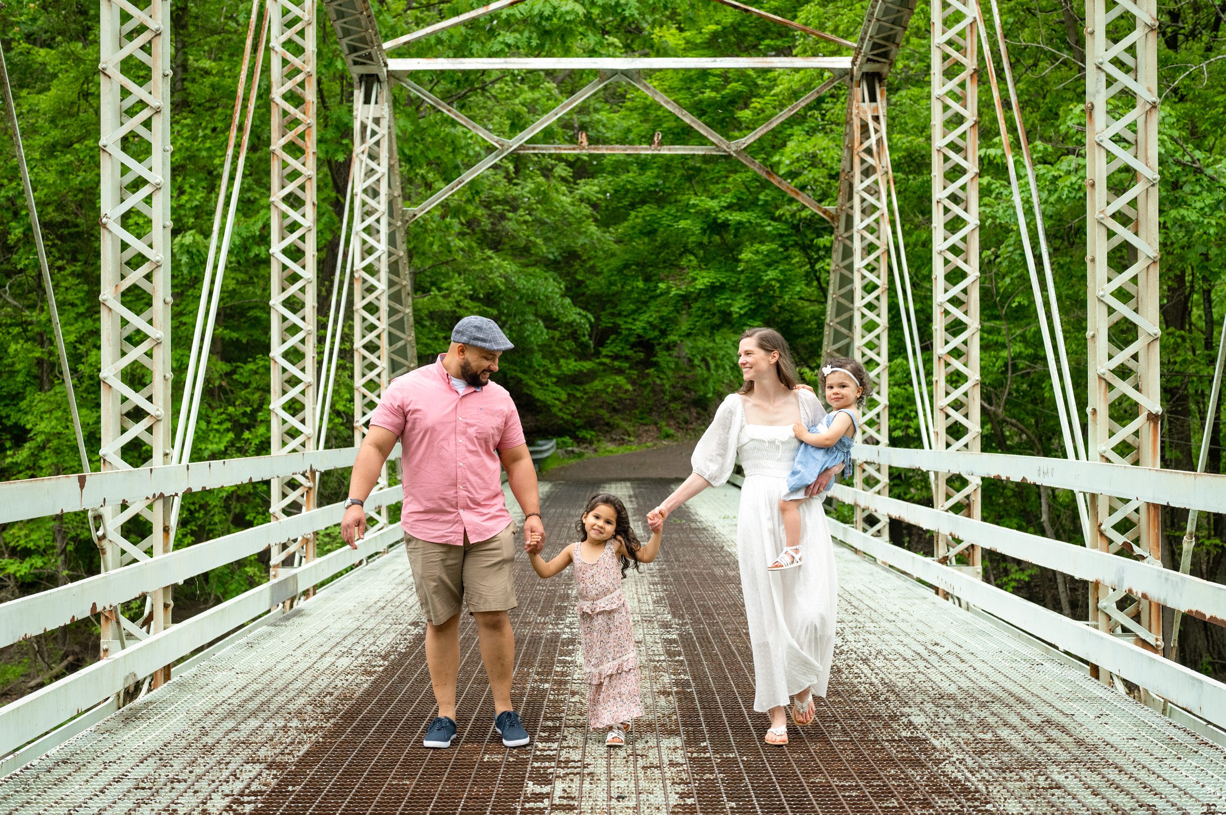 a family of four holding hands and walking along a bridge during a family photoshoot