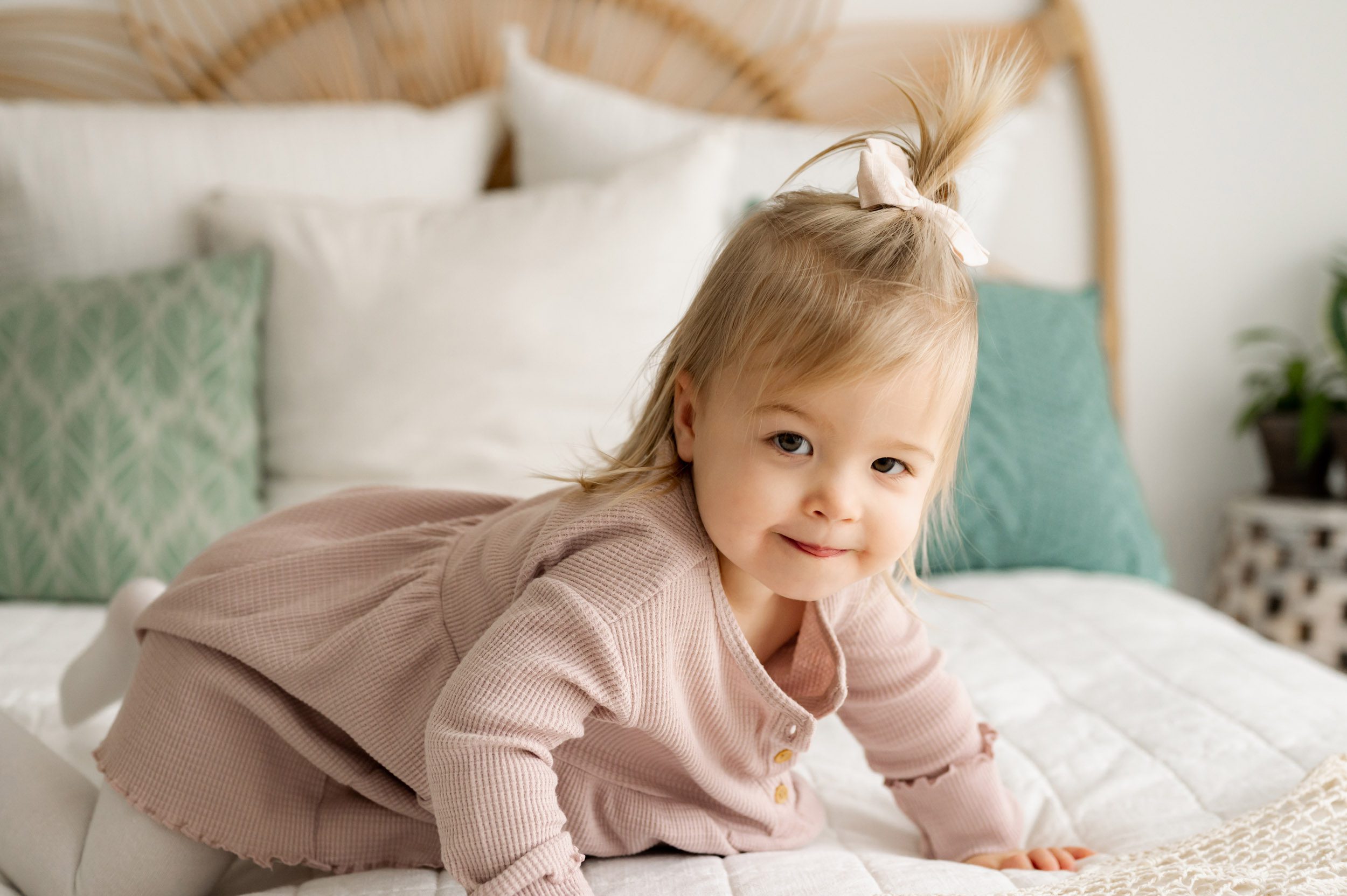 a young girl crawling across a bed and sticking her tongue out a tiny bit as she looks at the camera 