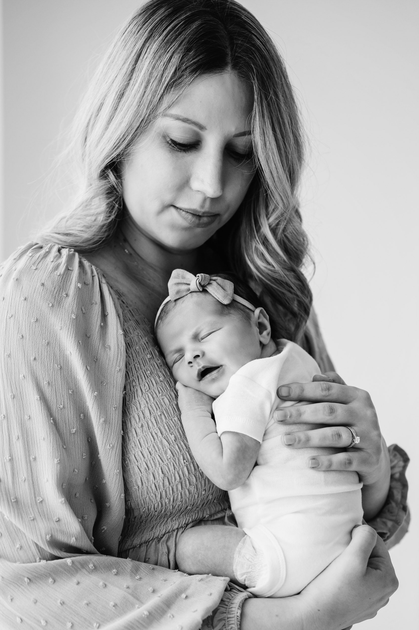 a black and white picture of a new mom holding her baby girl up against her chest and smiling down at her during a newborn photography session