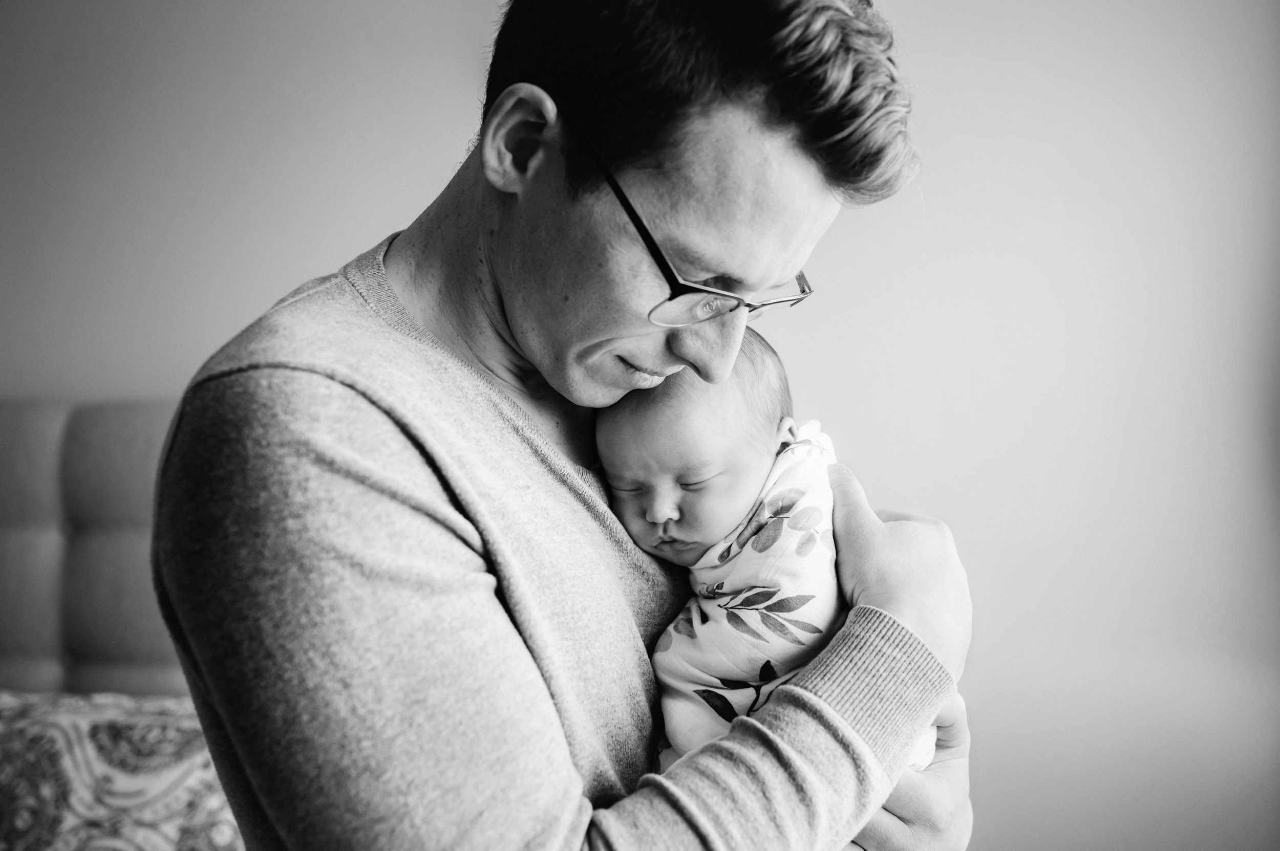 a black and white picture of a dad holding his baby girl against his chest and hugging her during an Exton in home newborn photography session