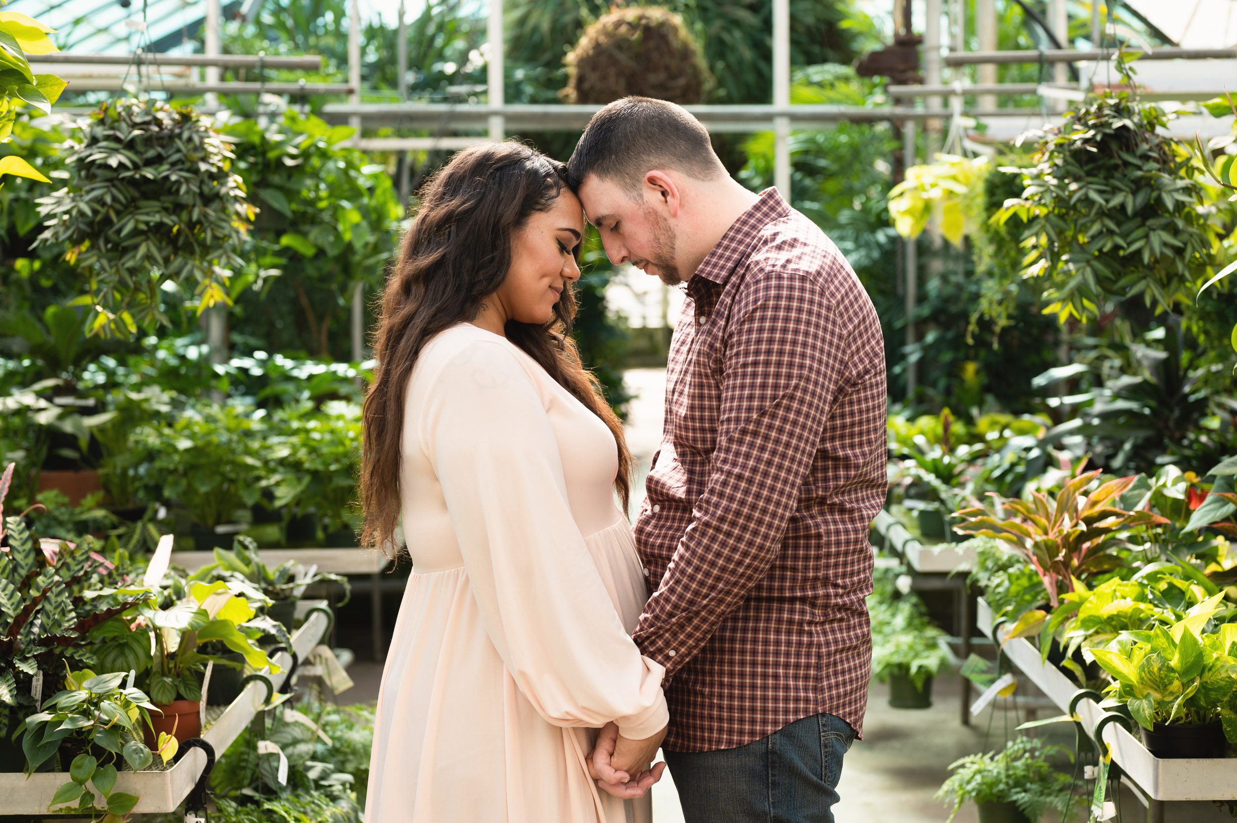 expecting parents standing in a greenhouse and resting their foreheads together during a Collegeville greenhouse maternity photography session