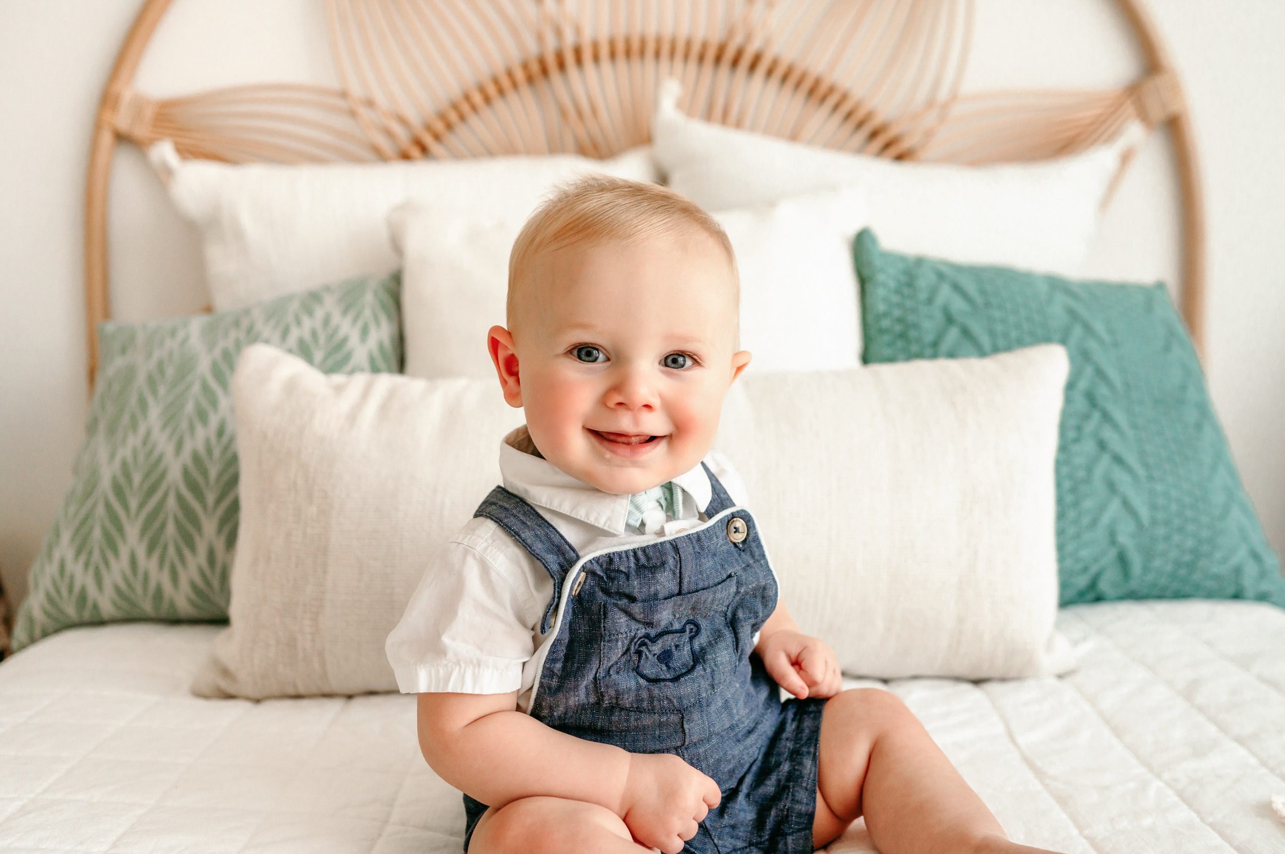 a baby boy sitting on a bed and smiling at the camera during a baby milestone photoshoot