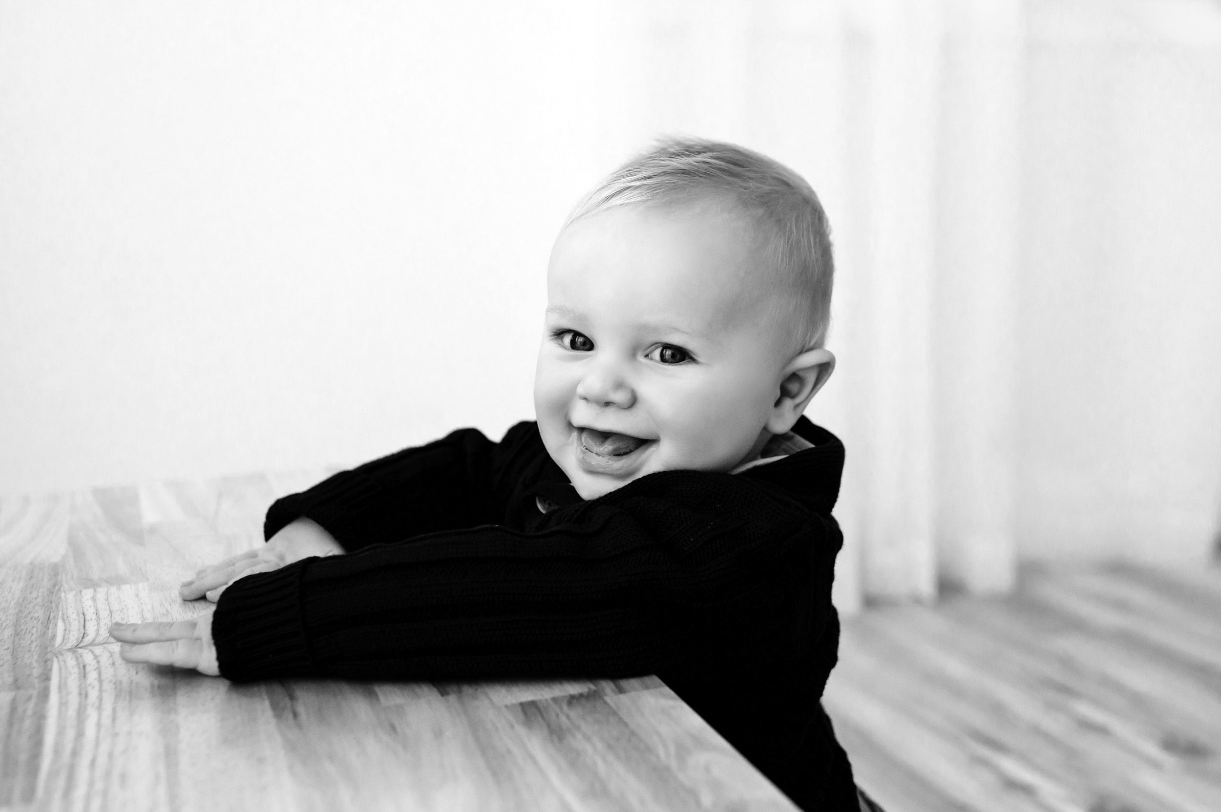 a black and white picture of a baby boy holding onto a wooden bench and smiling at the camera during a Pottstown baby milestone photography session
