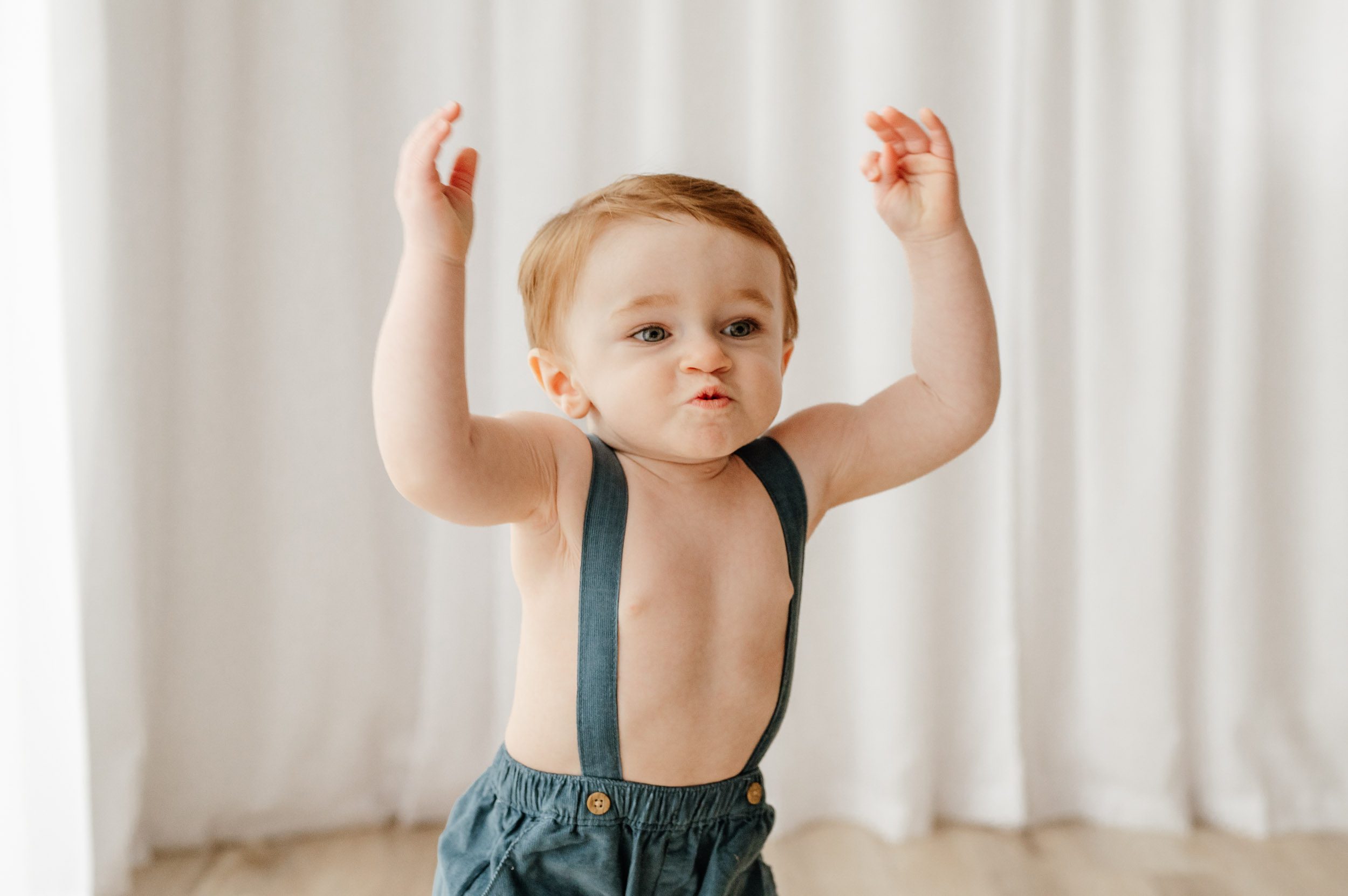 a little boy raising his hands up in the air and running with his lips pursed in determination during a toddler milestone photoshoot